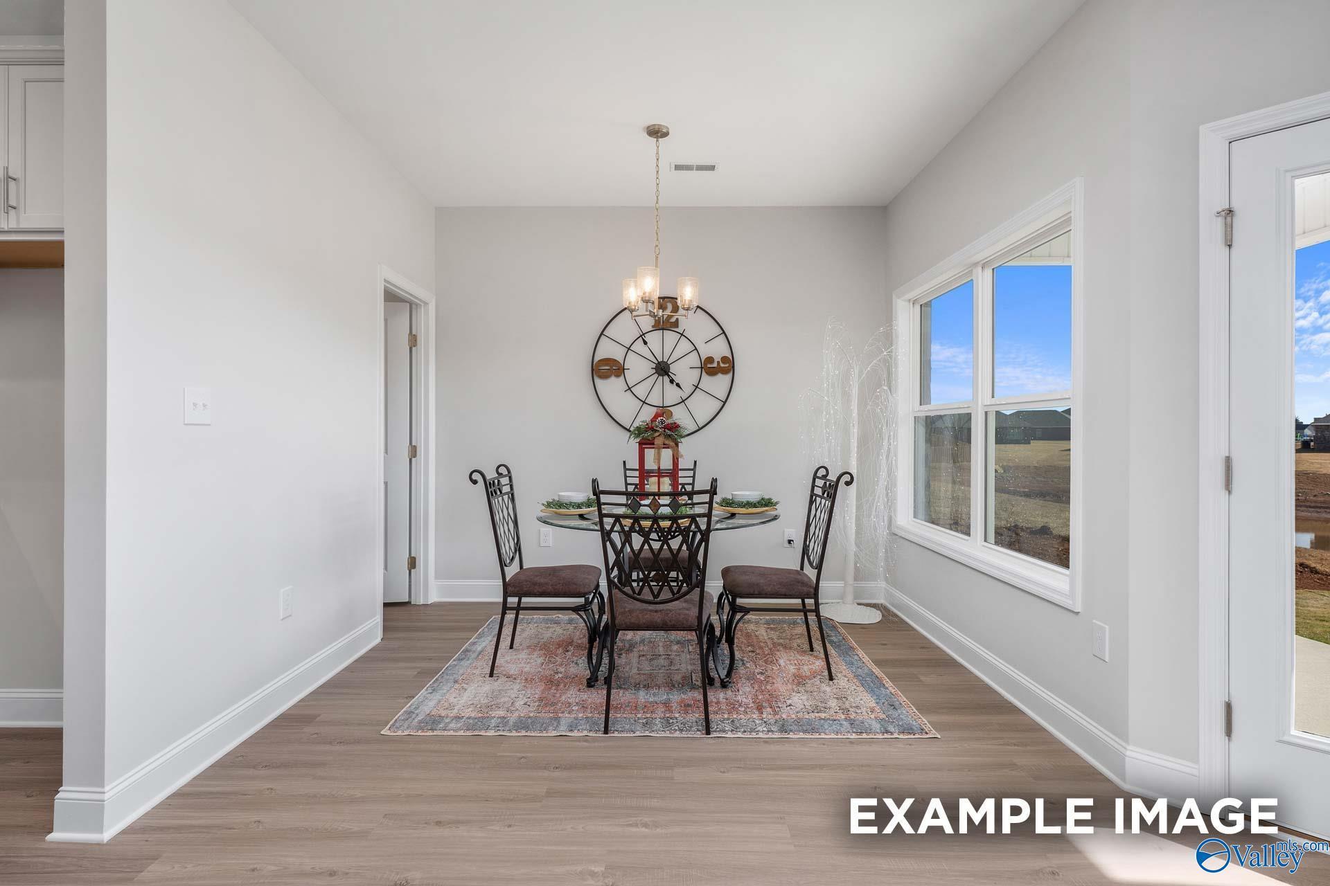 Elegant dining room with round glass table, ornate chairs, chandelier, and field views through large windows in The Daphne D home, Meridianville