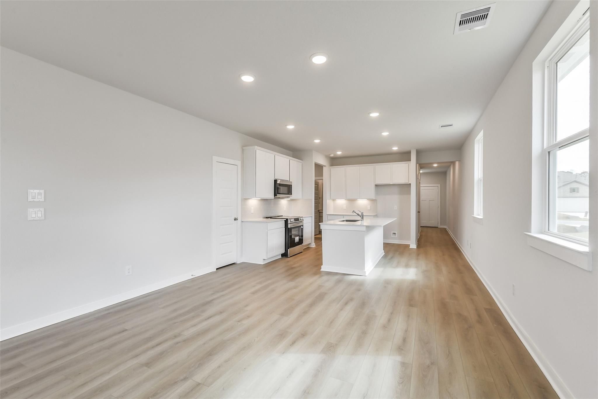 Modern open-concept kitchen with white cabinets, center island, stainless appliances, and hardwood floors in The Frio G home