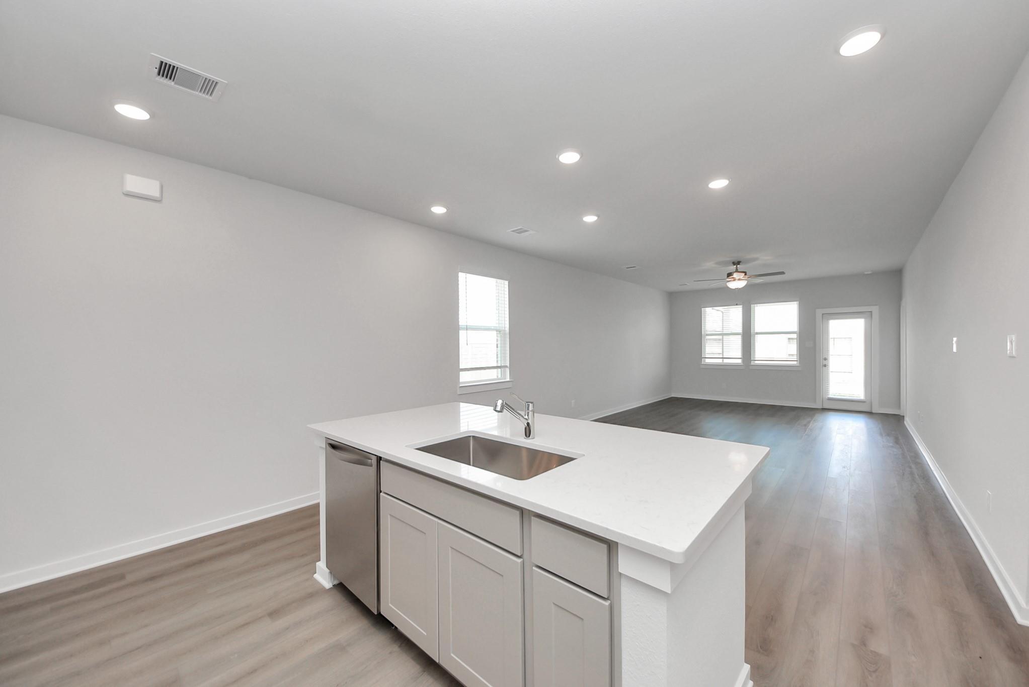 White kitchen island with sink overlooking open-concept living area in Davidson Homes The San Marcos E, Emberly, Beasley, Texas