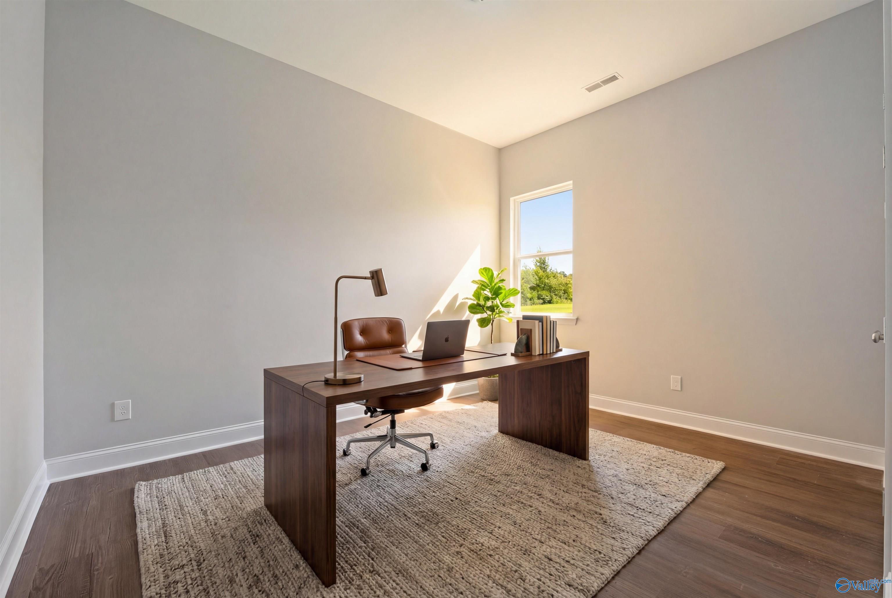 Modern home office with wooden desk, leather chair, laptop, plant, and natural light in The Arcadia B, Huntsville, AL
