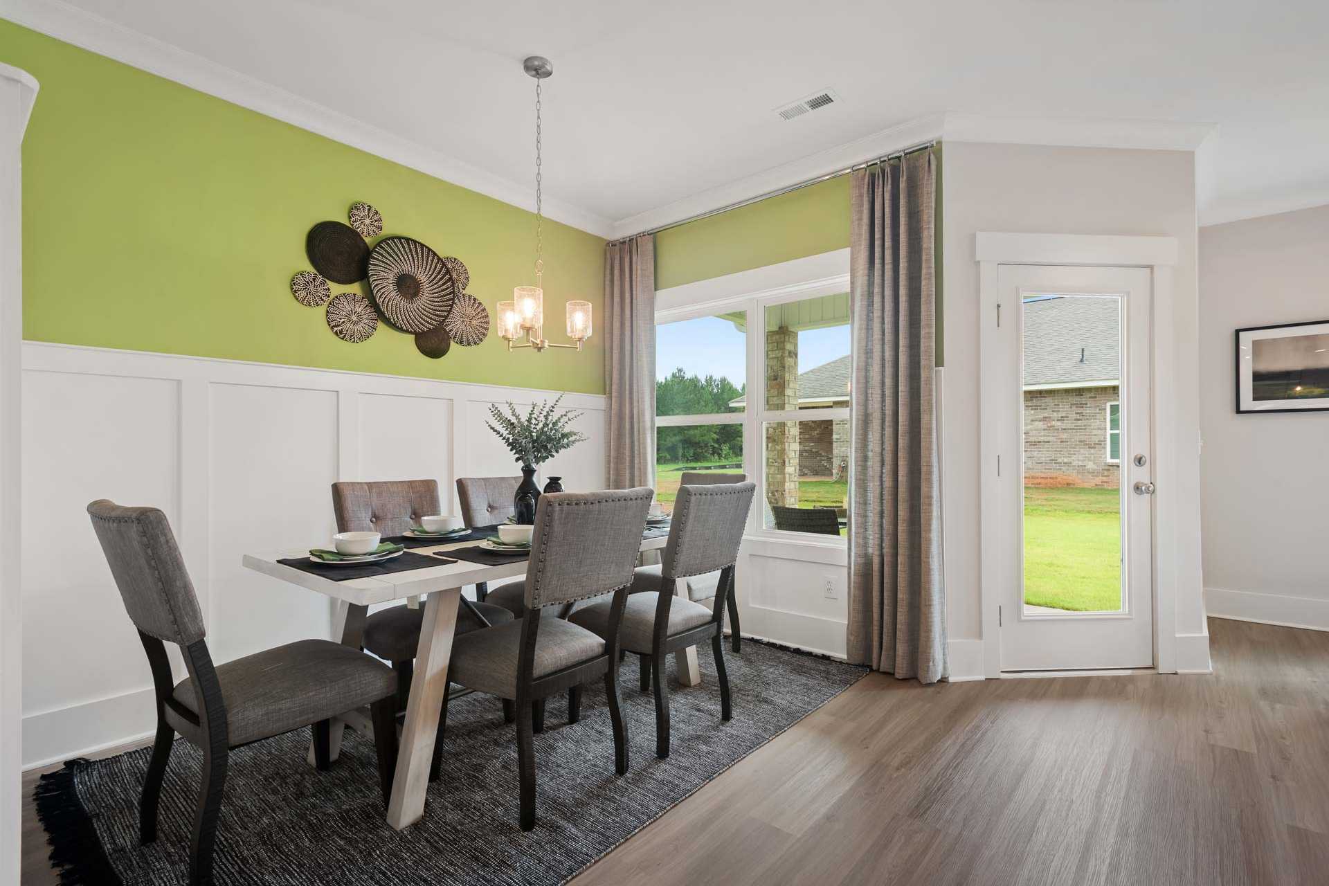Modern dining room at Durham Farms in Harvest Alabama with wooden table, gray chairs, green accent wall, wall art, and garden-view windows