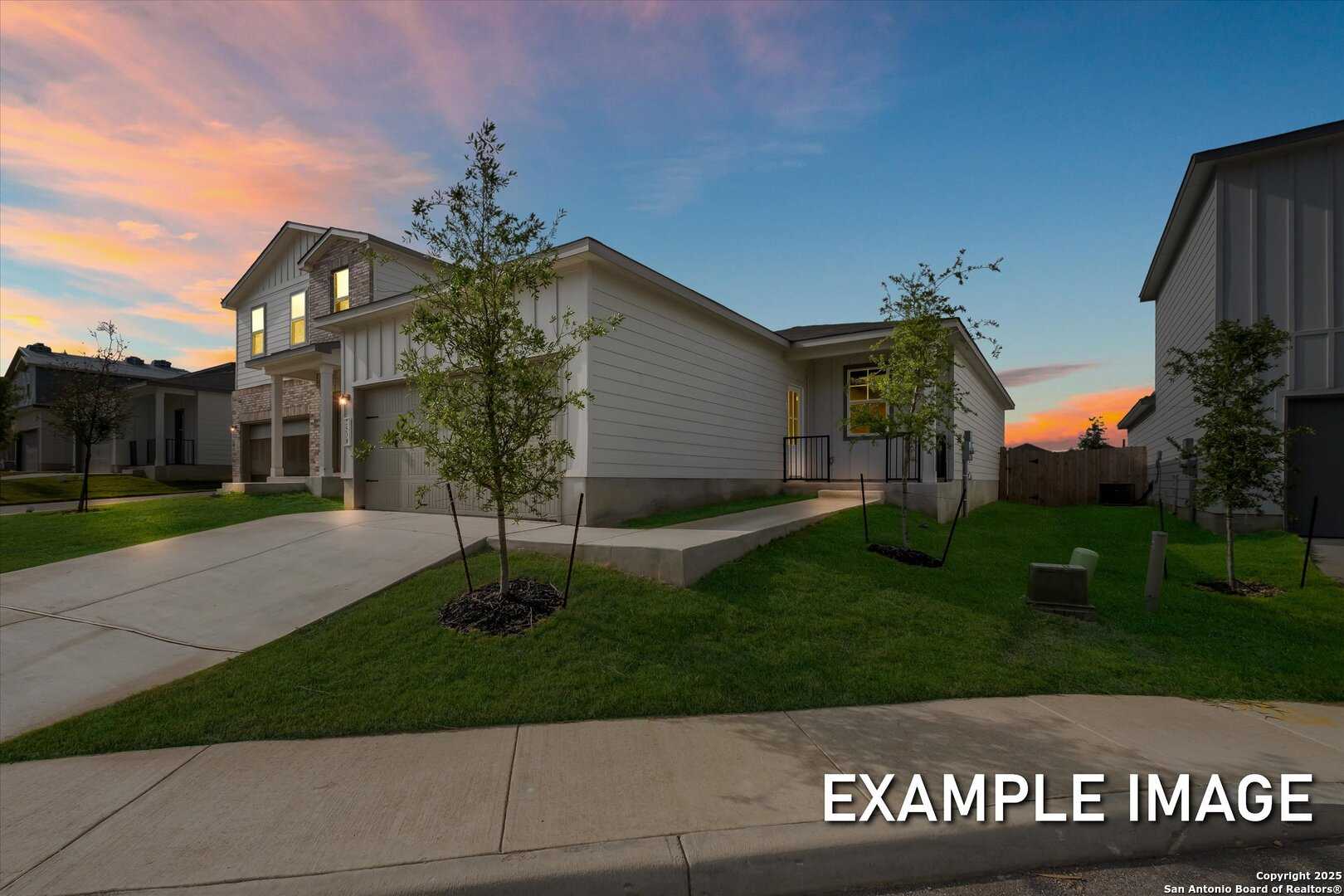 Modern 1-story Davidson Homes The Comal B with 2-car garage, driveway, and young trees in Agave, San Antonio, Texas at sunset