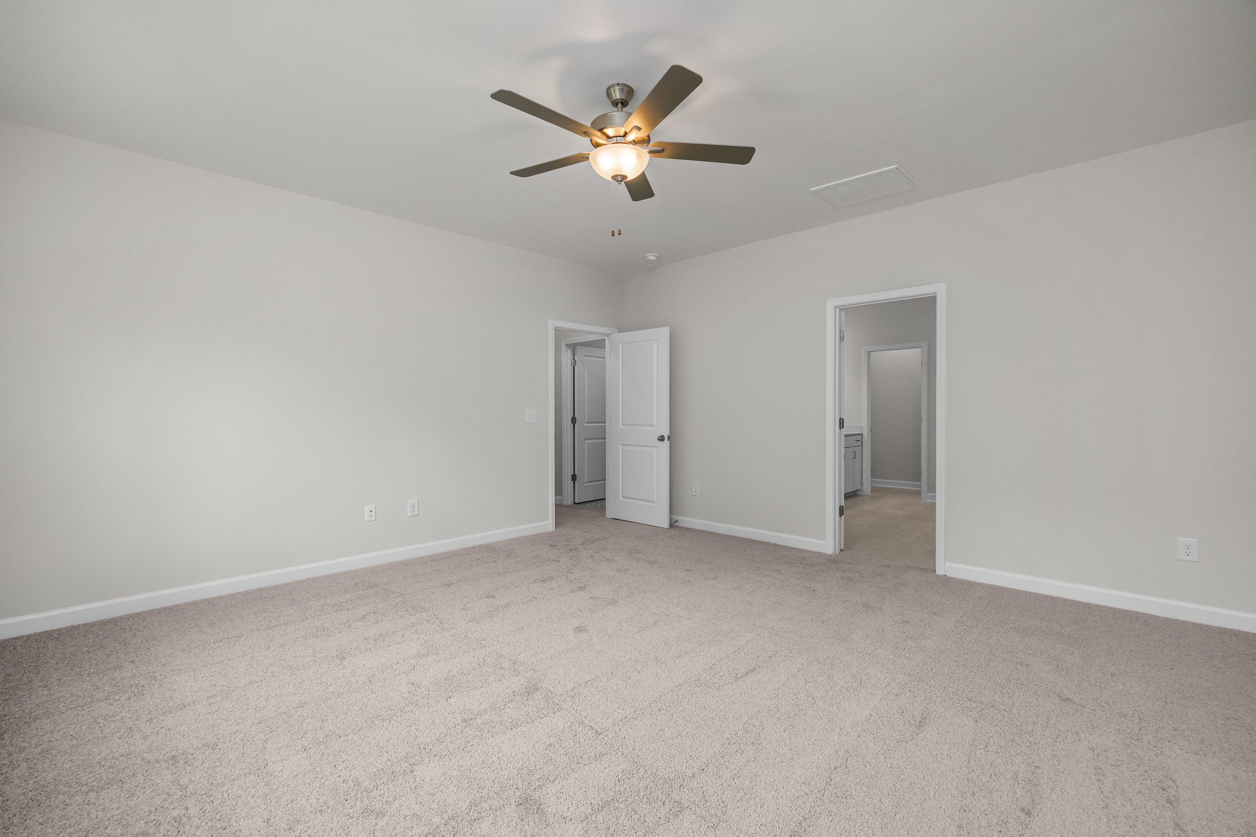Spacious master bedroom in The Aspen by Davidson Homes with ceiling fan, light gray walls, beige carpet, and open doorways