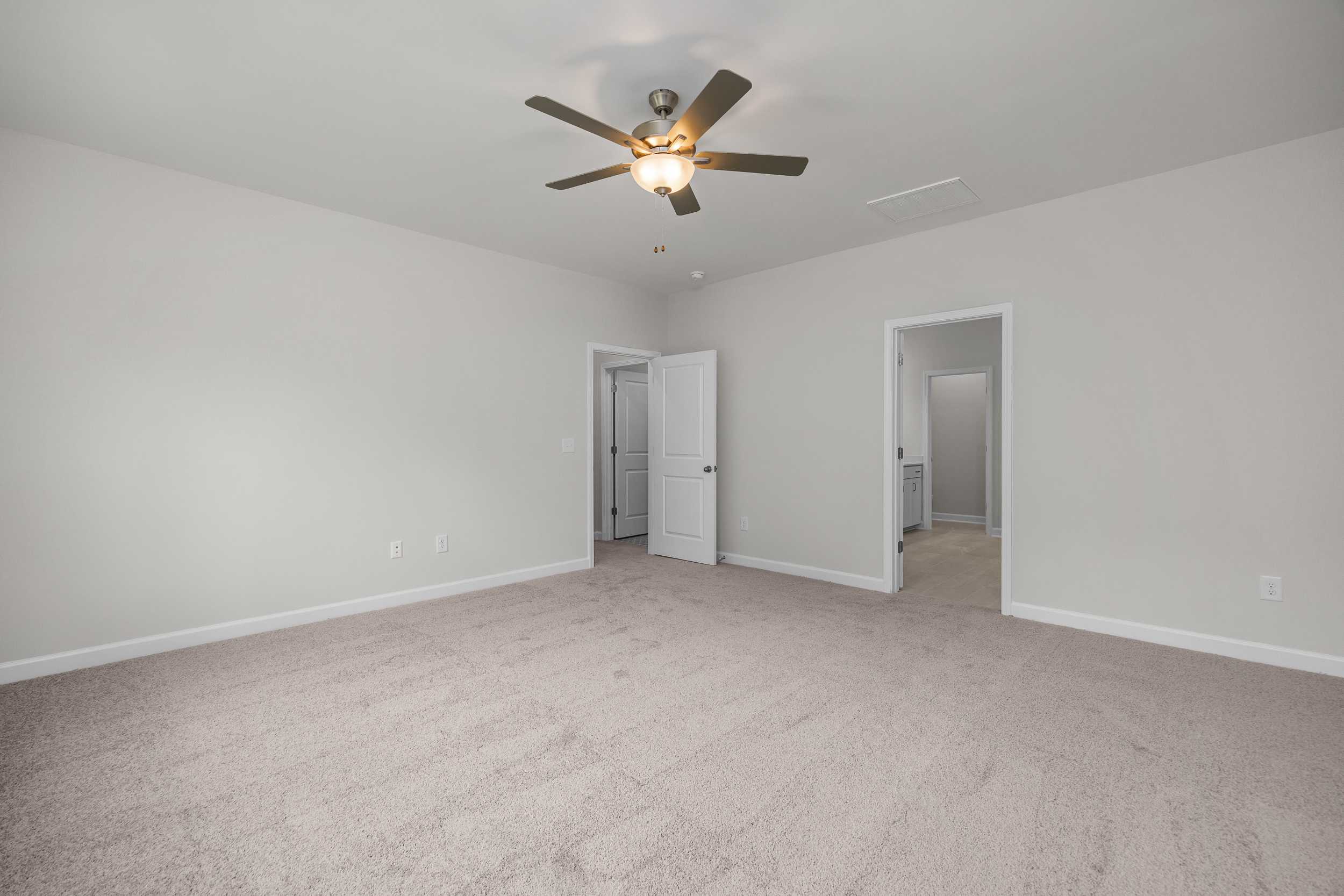 Spacious master bedroom in The Aspen by Davidson Homes with ceiling fan, light gray walls, beige carpet, and open doorways