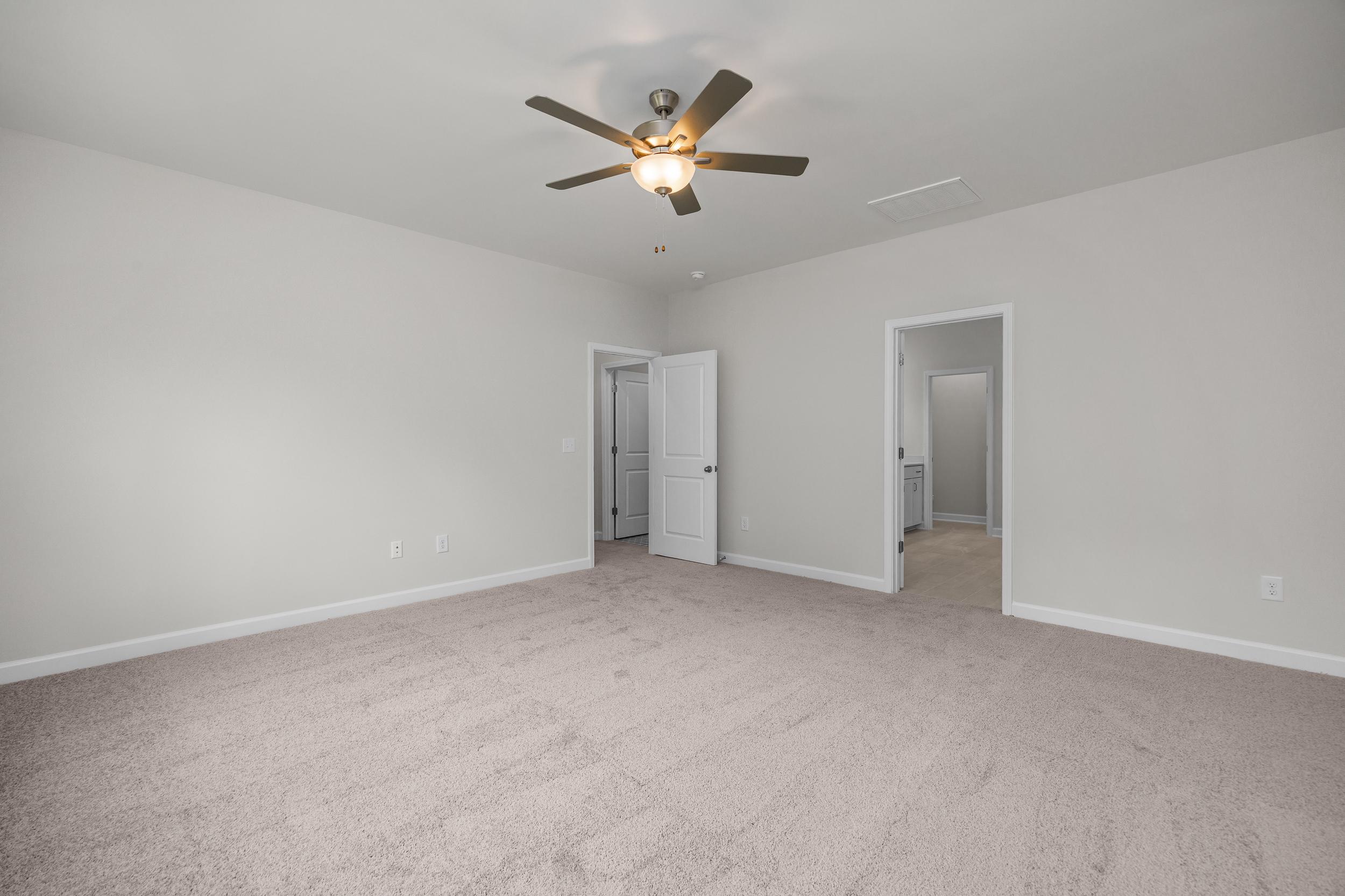 Spacious master bedroom in The Aspen by Davidson Homes with ceiling fan, light gray walls, beige carpet, and open doorways