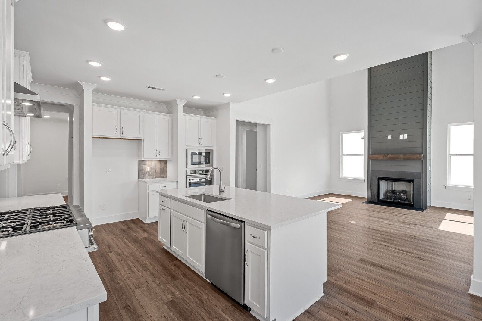 Modern open kitchen with white shaker cabinets, quartz island sink, stainless appliances, and stone fireplace in Davidson Homes The Hawkins, Murfreesboro