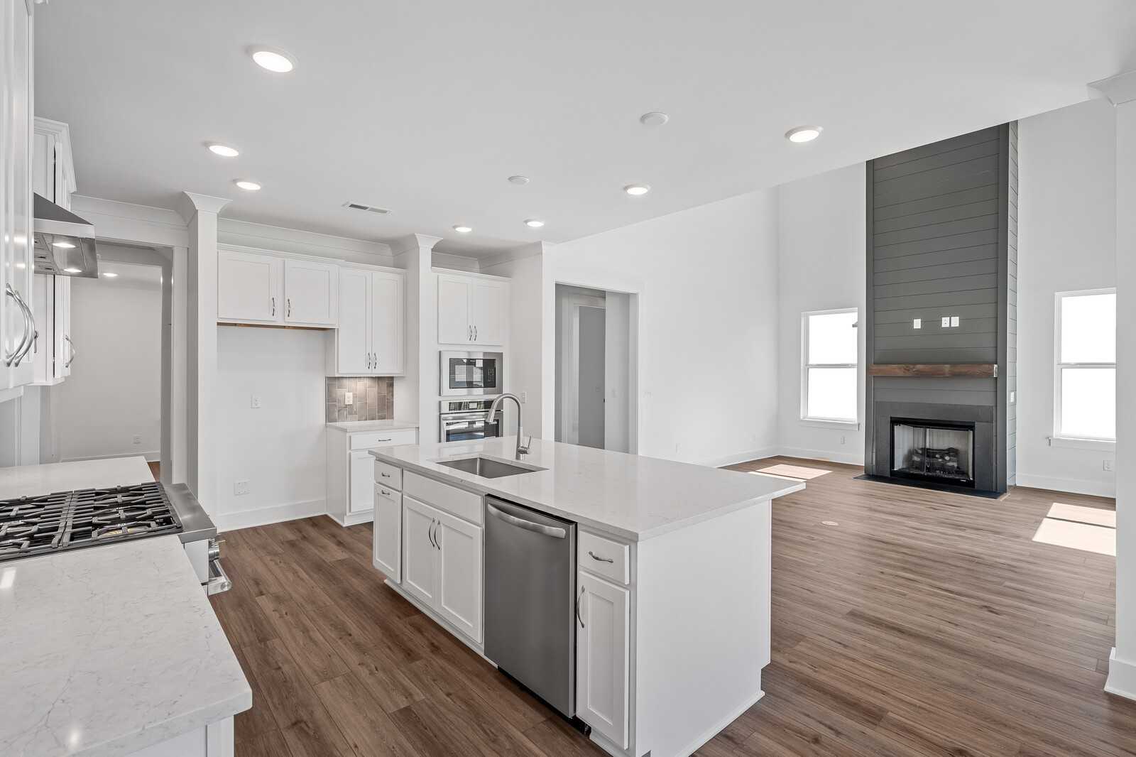 Modern open kitchen with white shaker cabinets, quartz island sink, stainless appliances, and stone fireplace in Davidson Homes The Hawkins, Murfreesboro