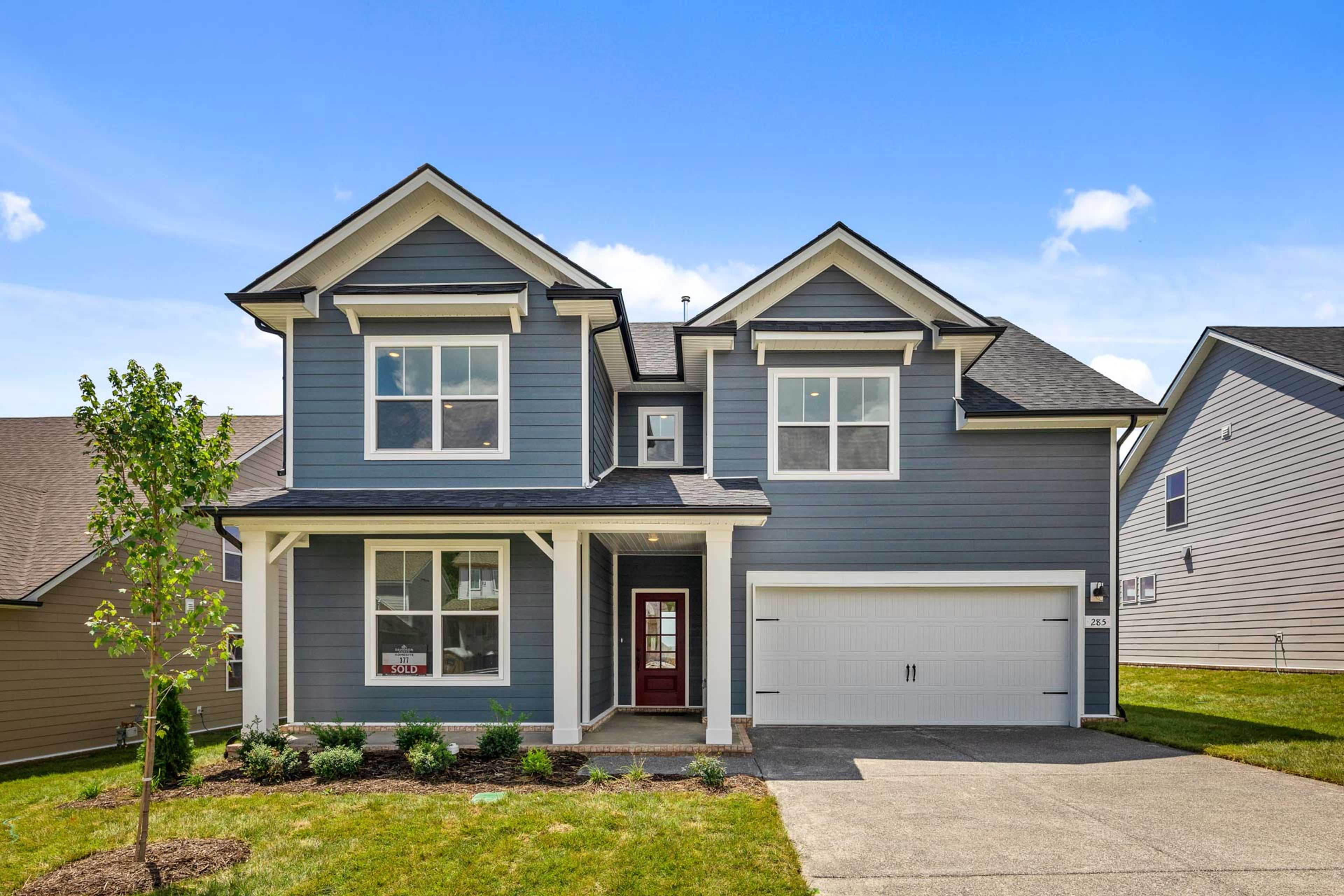 Two-story craftsman home with blue siding, covered front porch, red door, and garage at Carellton in Gallatin, Tennessee