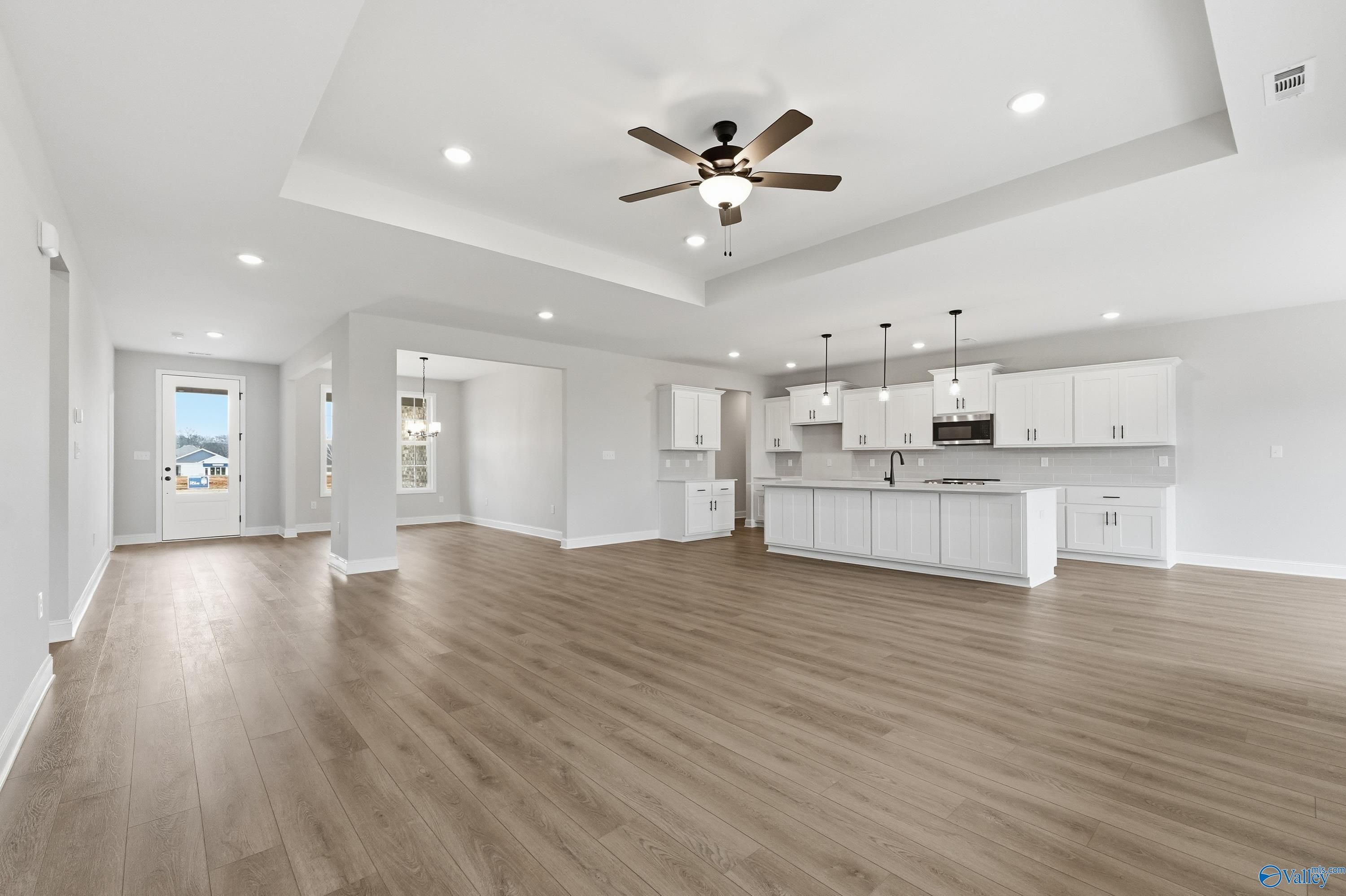 Open-concept kitchen and living area with white cabinets, island, hardwood floors, ceiling fan in The Finleigh by Davidson Homes, Meridianville AL