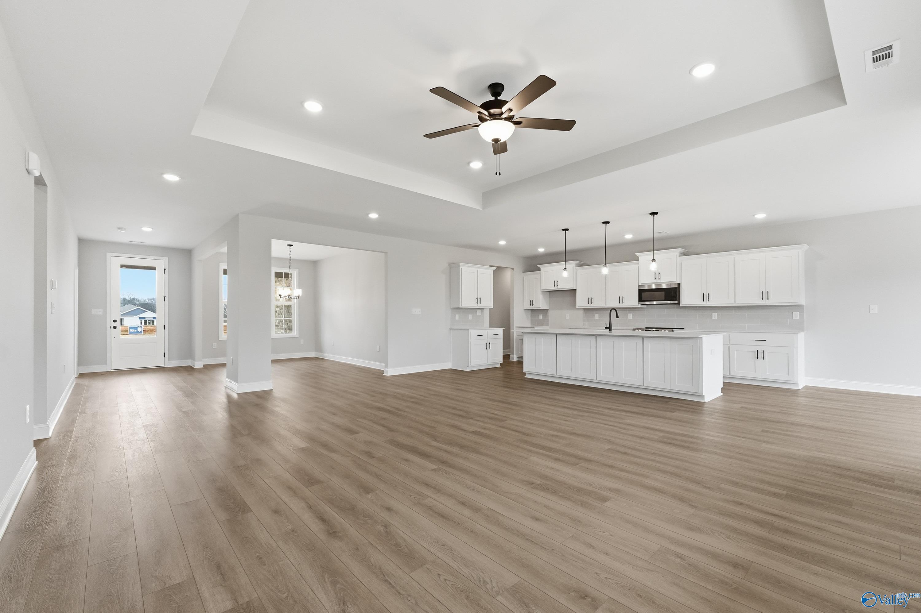 Open-concept kitchen and living area with white cabinets, island, hardwood floors, ceiling fan in The Finleigh by Davidson Homes, Meridianville AL