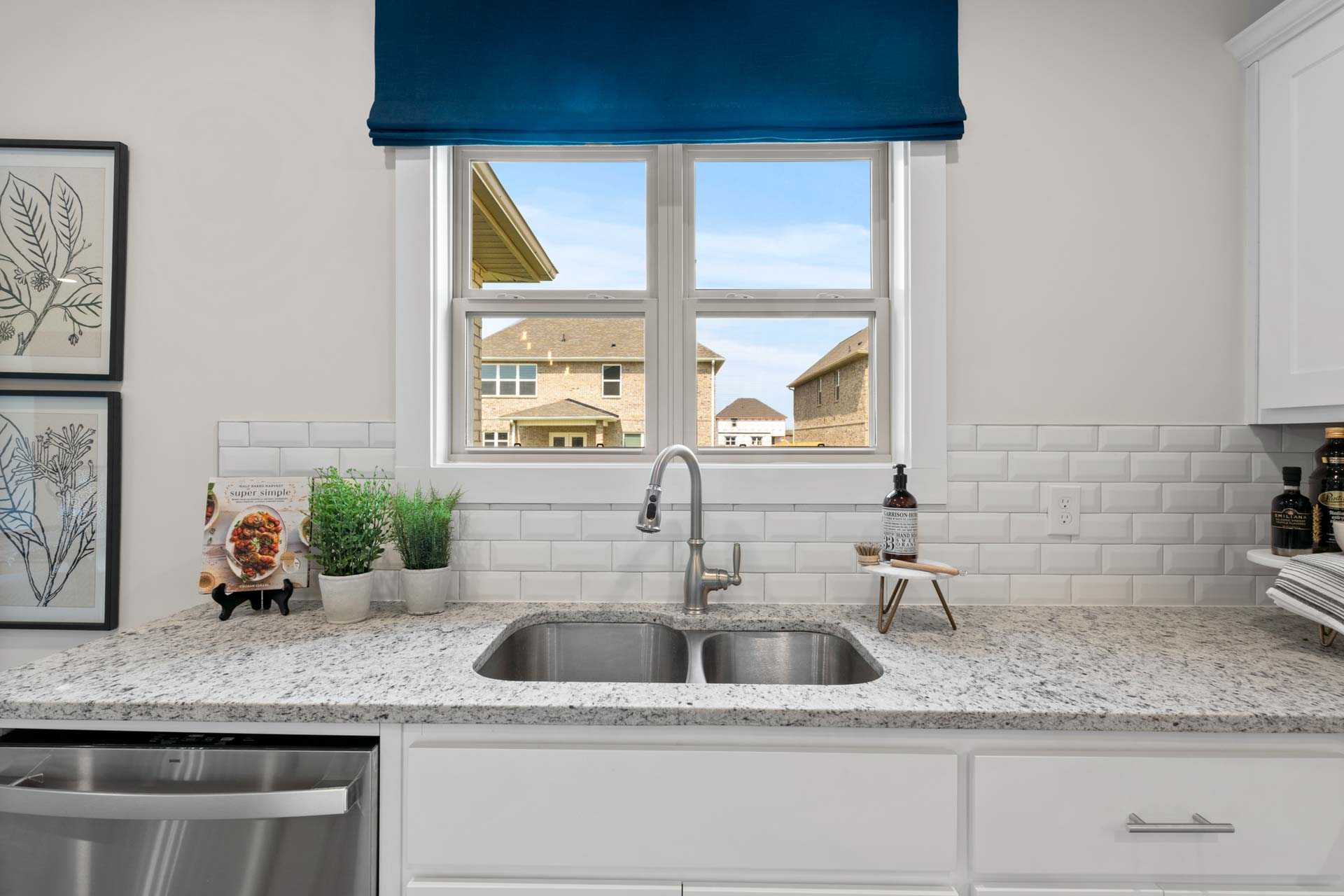 Spacious modern kitchen at Walker's Hill in Meridianville AL with white cabinets, granite counters, subway tile backsplash, and window view of neighborhood homes