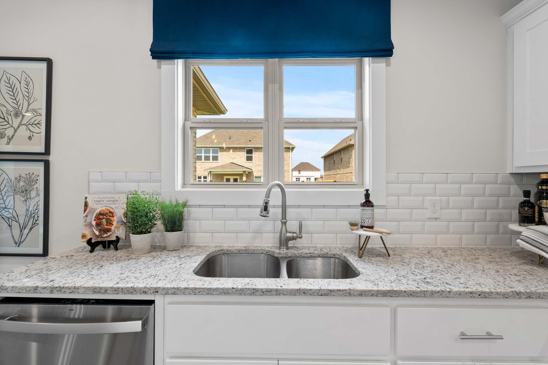 Spacious modern kitchen at Walker's Hill in Meridianville AL with white cabinets, granite counters, subway tile backsplash, and window view of neighborhood homes