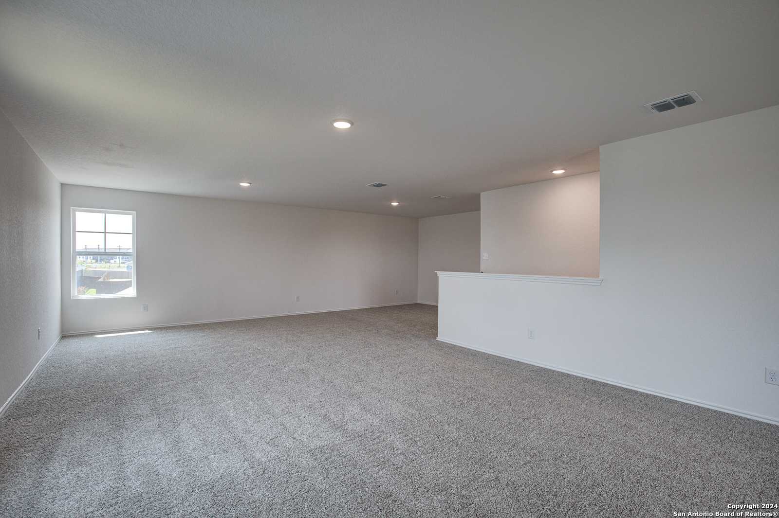 Spacious upstairs loft with gray carpet, white walls, large window, and overlooking railing in Davidson Homes The Douglas D, Seguin, Texas