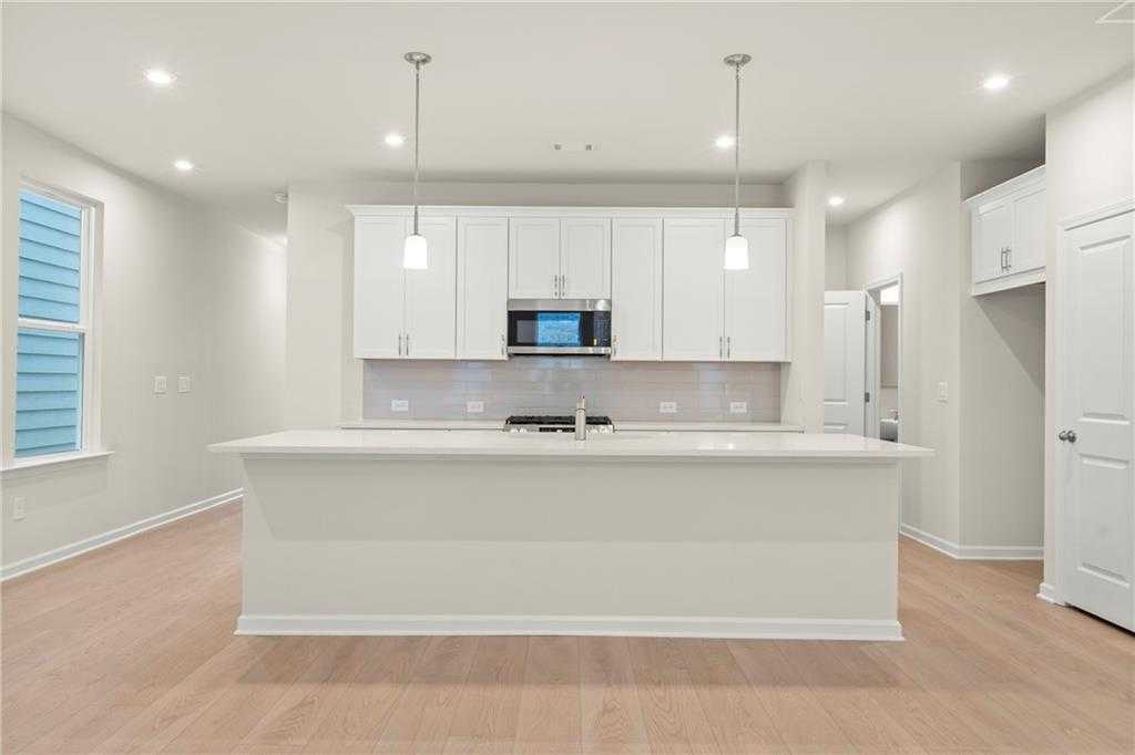 Modern white kitchen with quartz island, stainless appliances, pendant lights in Davidson Homes The Cary A, Kennesaw, Georgia