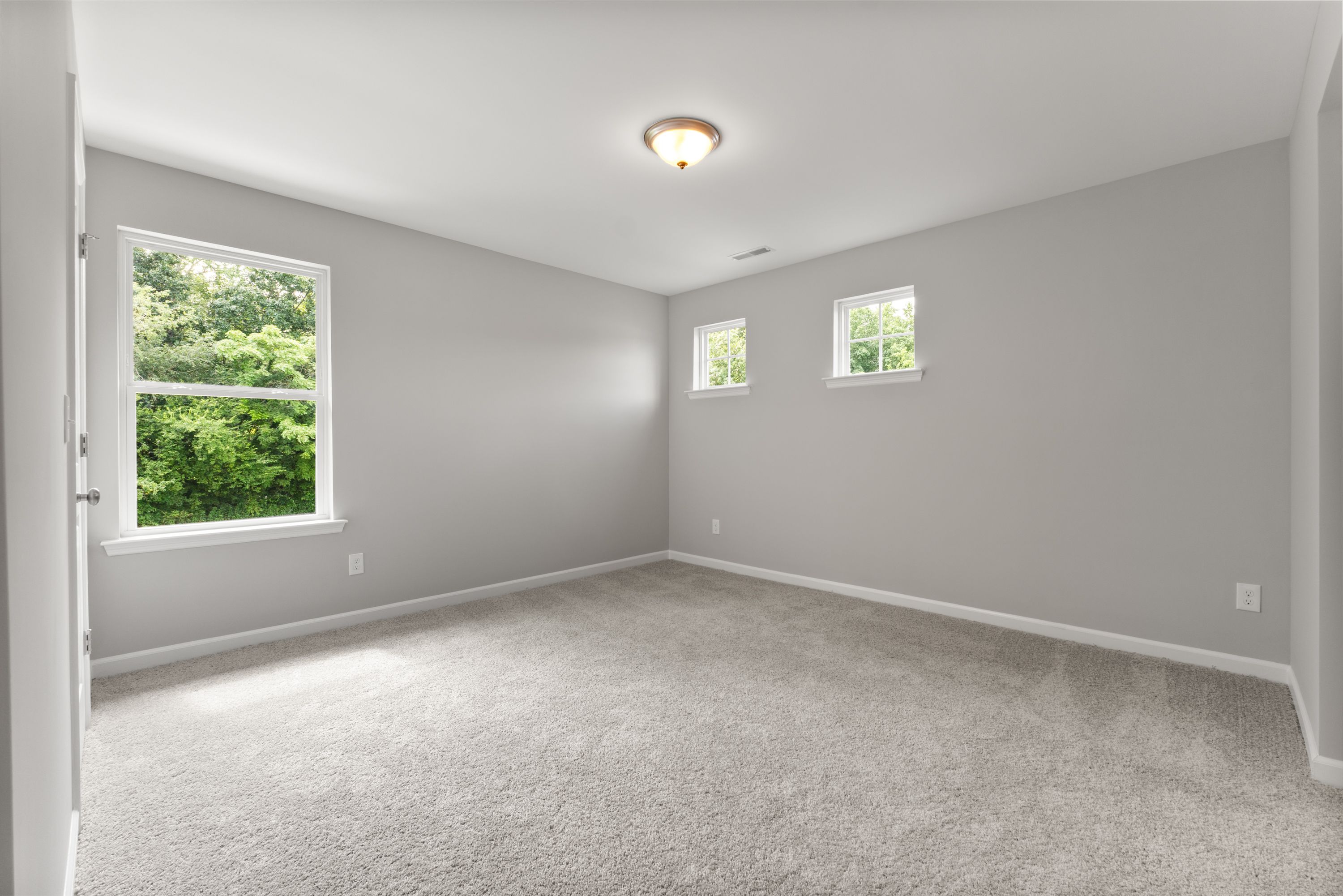 Spacious secondary bedroom in The Avalon E with light gray walls, carpeted floor, and tree-view windows