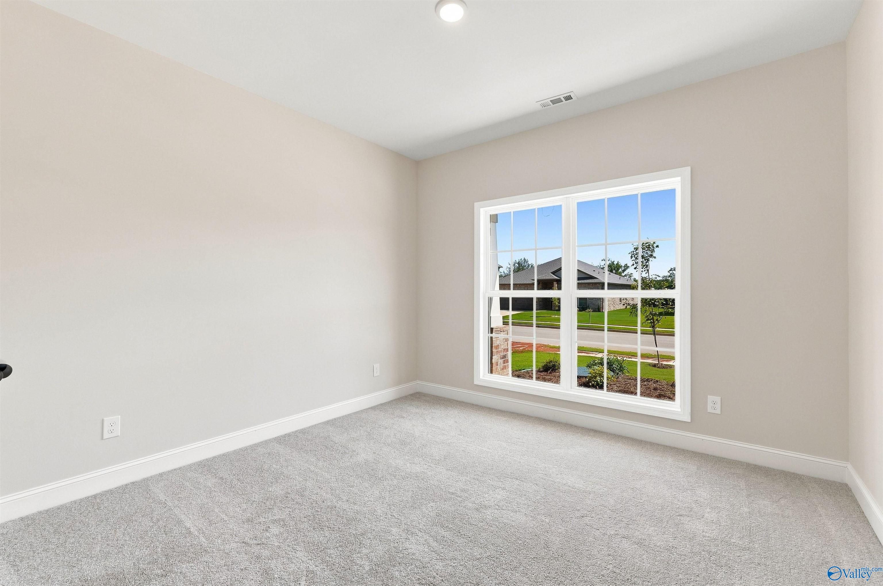 Bright carpeted bedroom with large double-pane window overlooking front yard in Davidson Homes The Everett B, Toney, Alabama