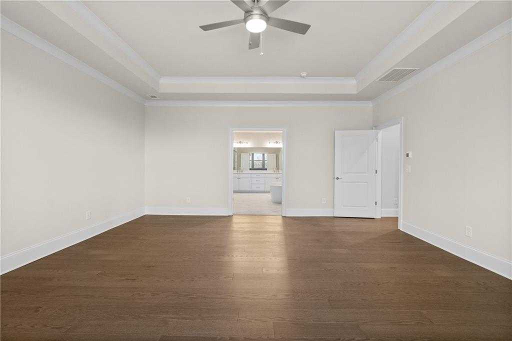 Spacious empty bedroom with tray ceiling, ceiling fan, hardwood floors, and open en-suite bathroom in Davidson Homes The Arlington A, East Cobb