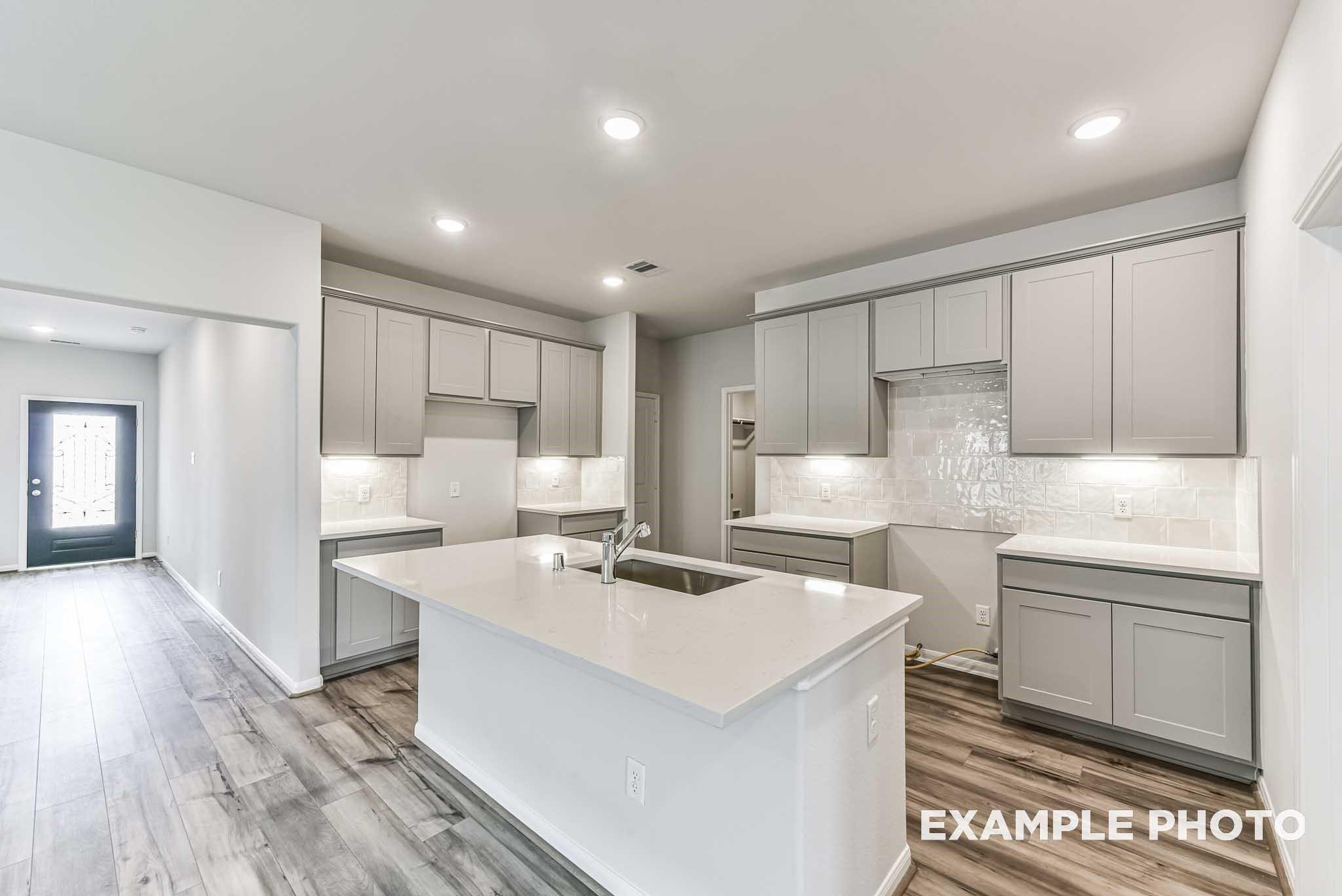 Modern kitchen with grey cabinets, quartz island, and wood-look flooring in The Laguna C floor plan, Sunterra, Katy, TX.