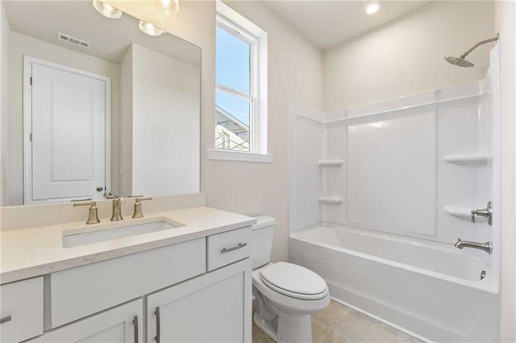 Bright secondary bathroom with white vanity, gold fixtures, tub-shower combo in Davidson Homes The Hampton C, Buford, GA