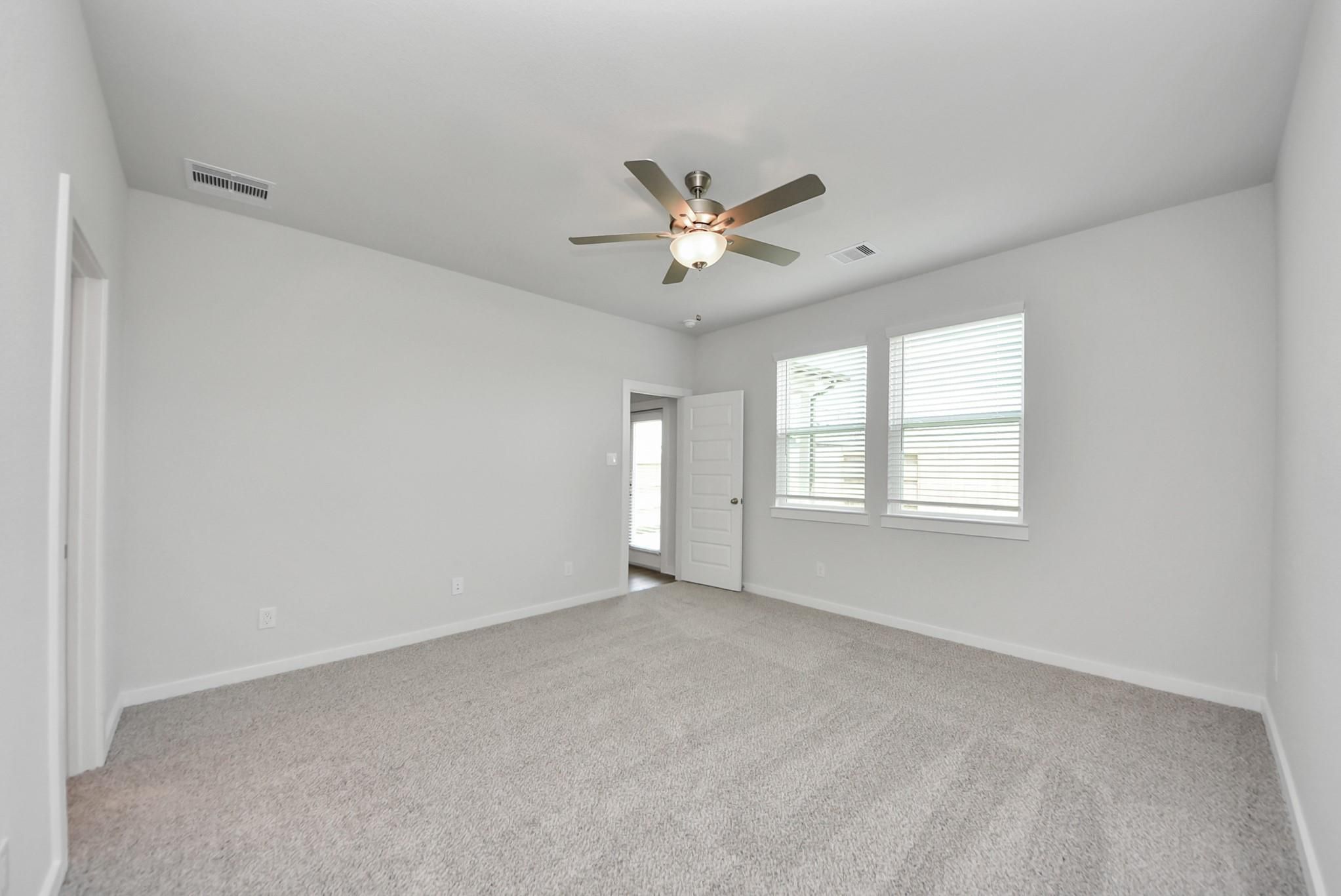 Spacious bright bedroom with ceiling fan, carpet flooring, and two windows in Davidson Homes The San Marcos E, Beasley, Texas
