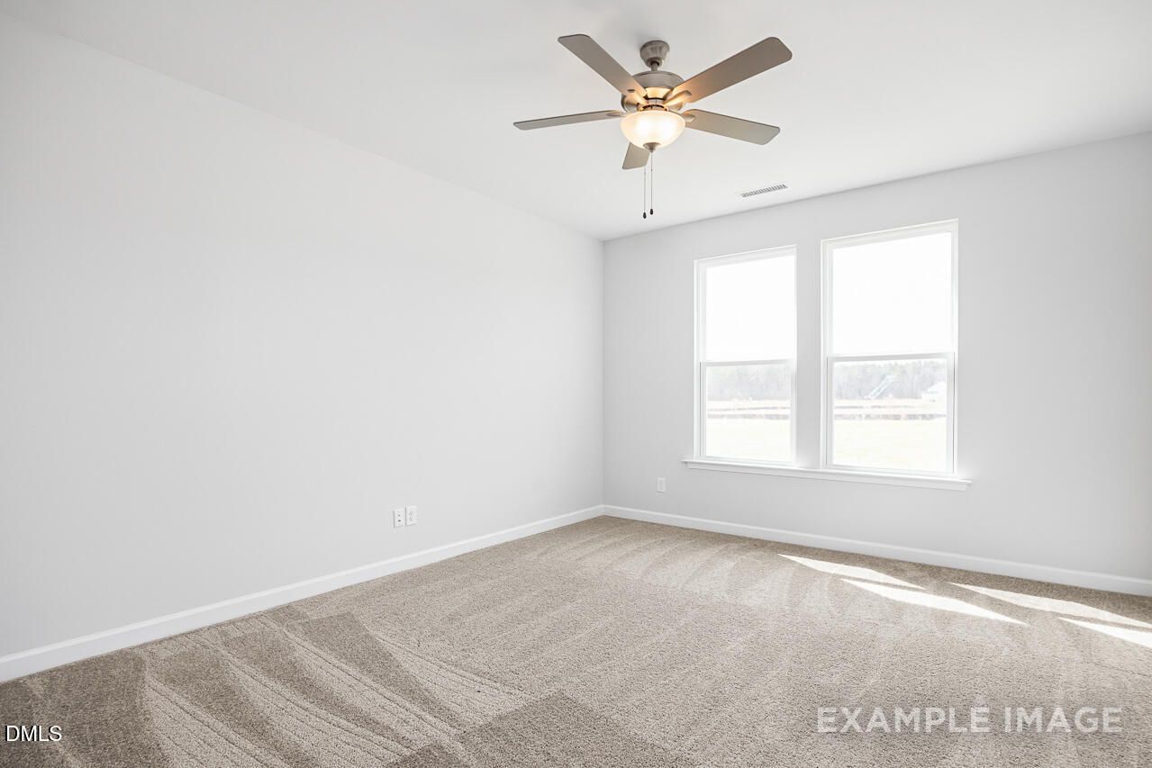 Bright empty bedroom with white walls, double windows, ceiling fan, and beige carpet in Davidson Homes The Daphne C, Lillington, NC