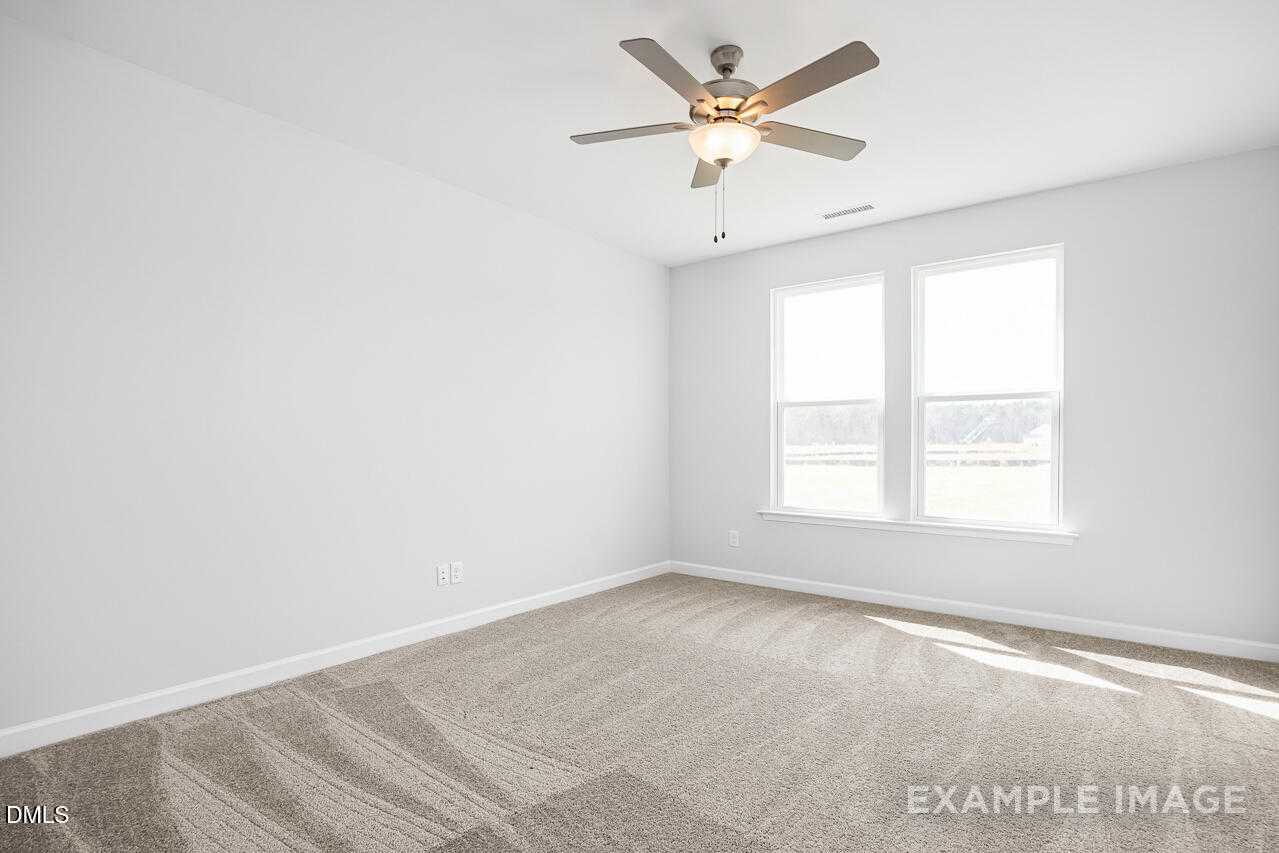 Bright empty bedroom with white walls, double windows, ceiling fan, and beige carpet in Davidson Homes The Daphne C, Lillington, NC