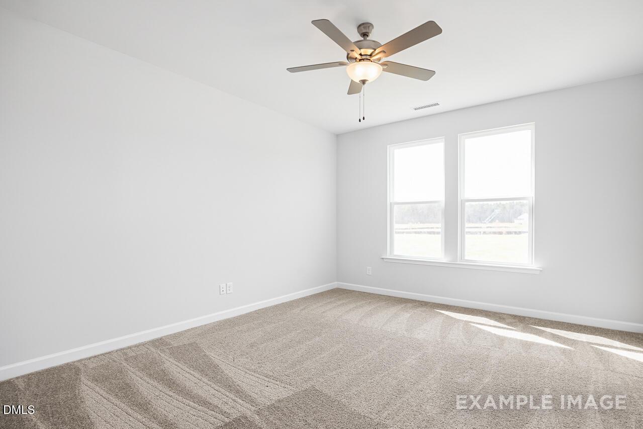 Bright secondary bedroom with ceiling fan, white walls, beige carpet, and large windows in Davidson Homes The Daphne C, Zebulon, NC