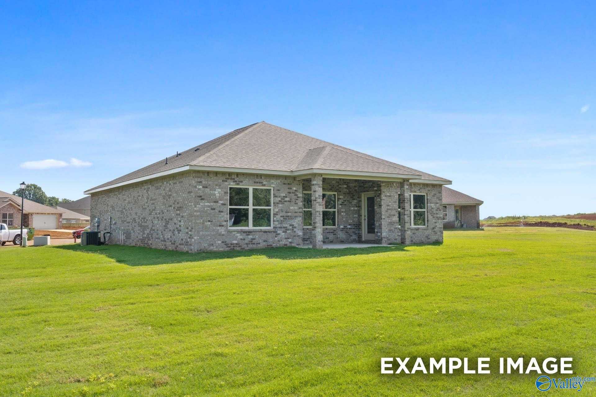Modern single-story stone home with covered porch, large windows, and lush green yard in The Highlands, Arab, Alabama - Davidson Homes The Asheville