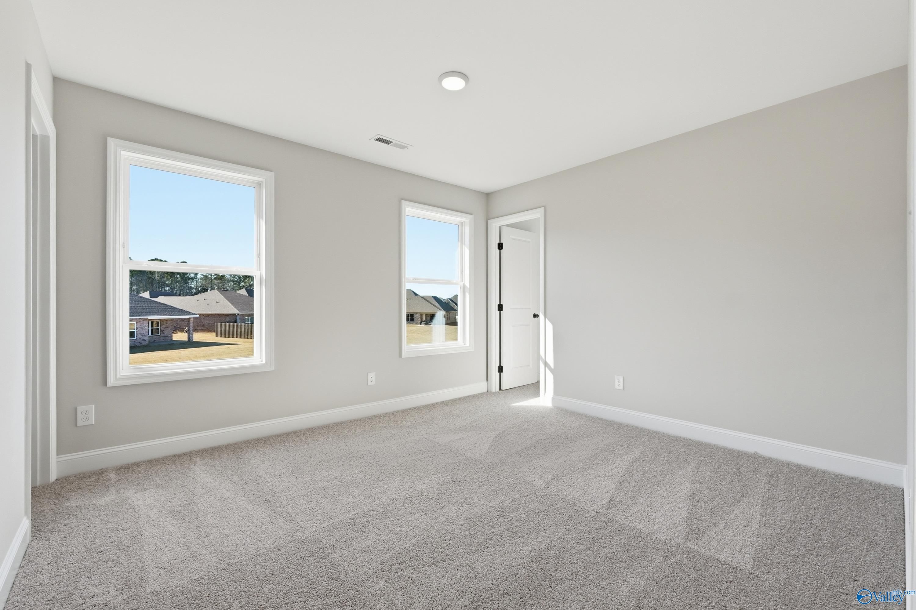 Spacious empty bedroom with light gray walls, large sunny windows, and plush carpet in Davidson Homes The Chelsea C, Harvest, AL