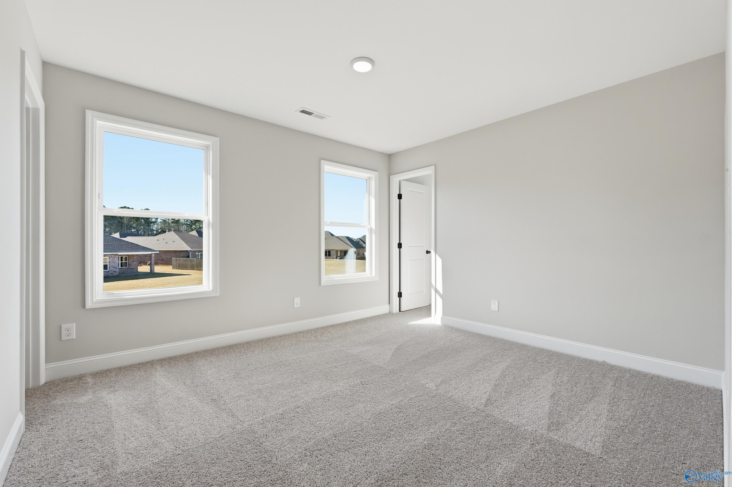 Spacious empty bedroom with light gray walls, large sunny windows, and plush carpet in Davidson Homes The Chelsea C, Harvest, AL