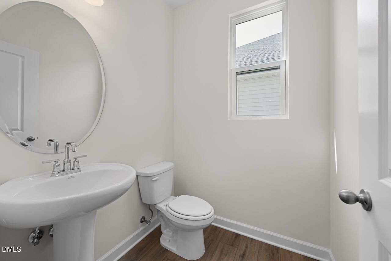 Bright bathroom with pedestal sink, round mirror, and toilet in Davidson Homes The Willow B, Woodland Crossing, Zebulon, NC