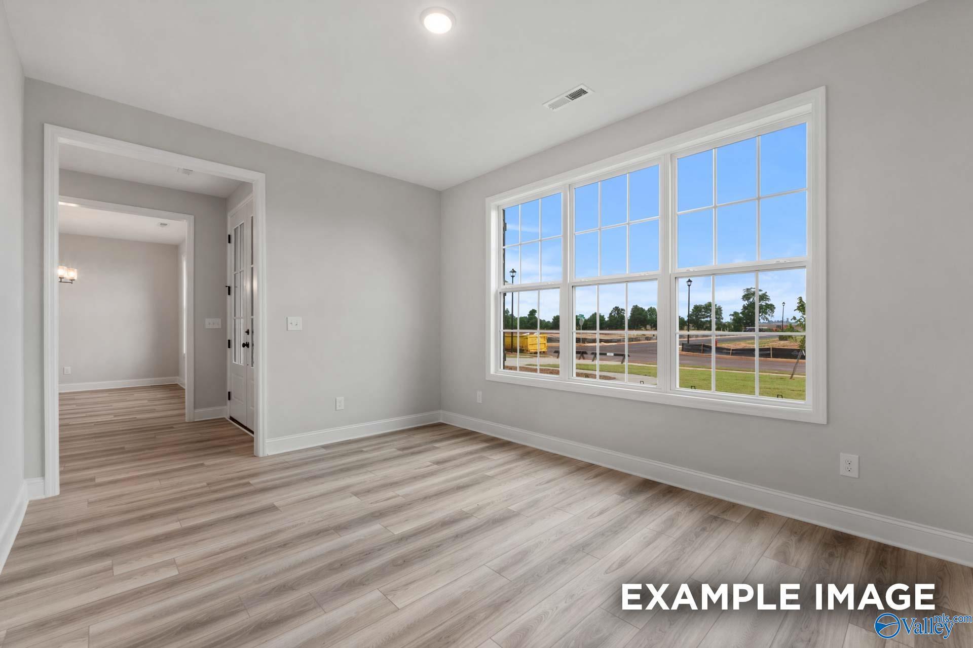 Bright living room with light wood floors and large windows overlooking green field in The Finleigh floor plan, Meridianville, Alabama