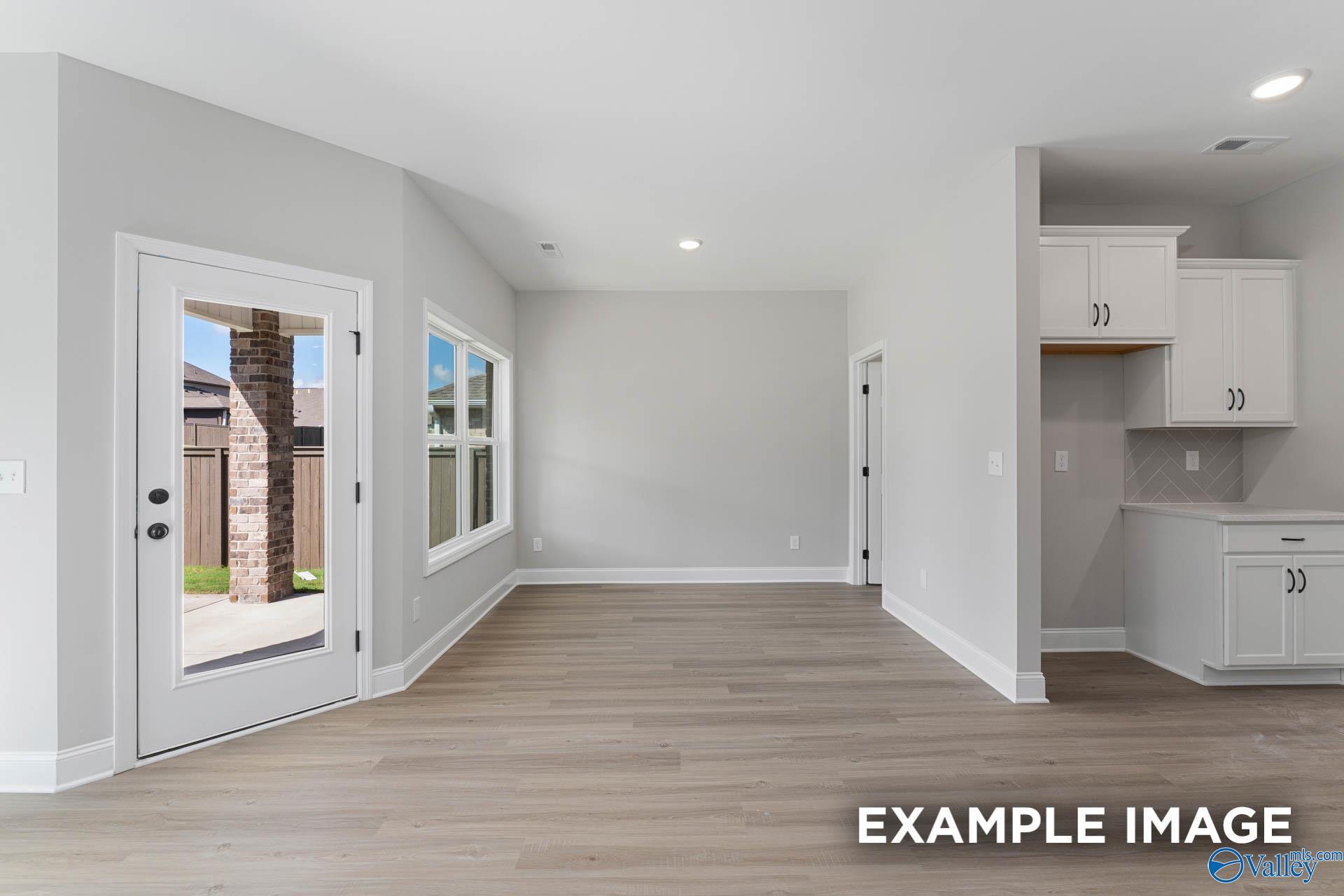 Open-concept living room with French doors to patio, large windows, and white kitchen cabinets in The Daphne D, Meridianville home