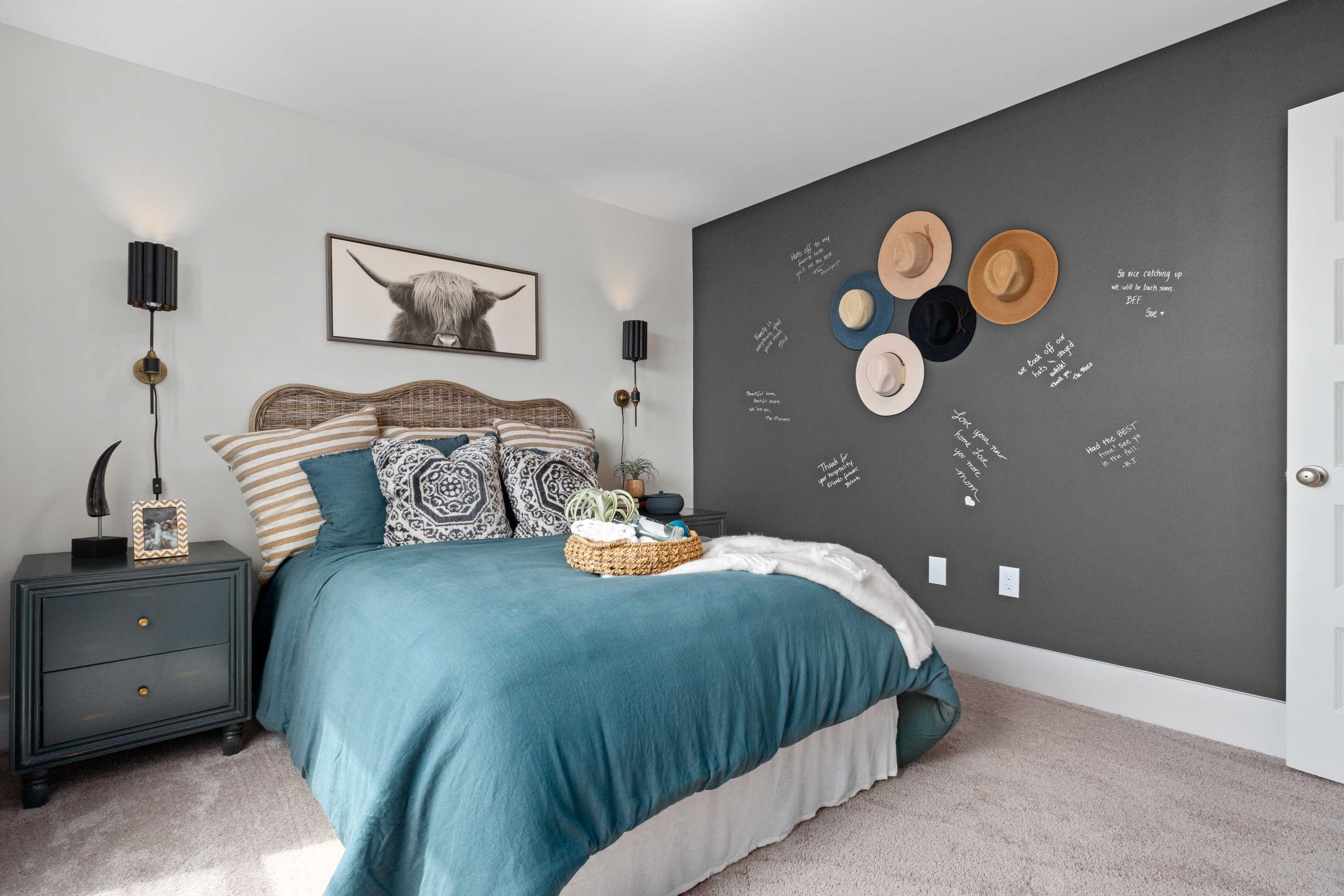 Cozy bedroom in Watts Glen featuring teal bedding, rattan headboard, wall hats, chalkboard messages, and Highland cow art in Owens Cross Roads, Alabama