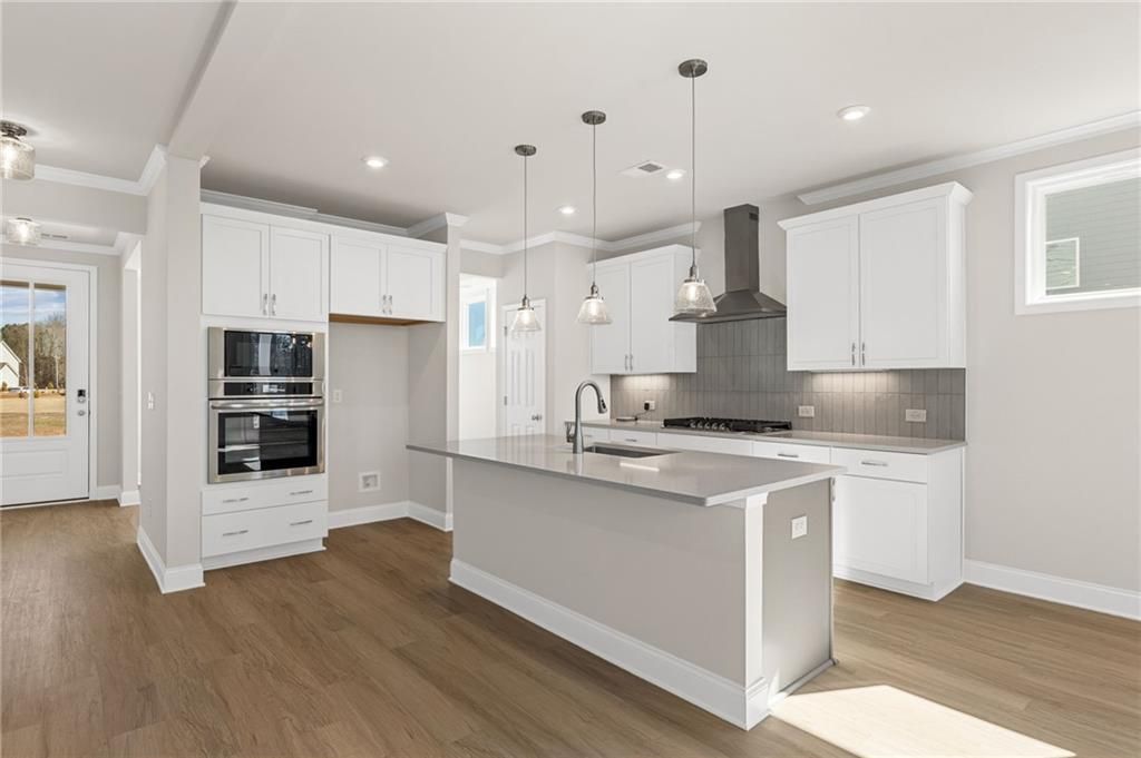 Bright open-concept kitchen with white shaker cabinets, stainless steel appliances, gray quartz island in Davidson Homes The Willow B, Hoschton, Georgia