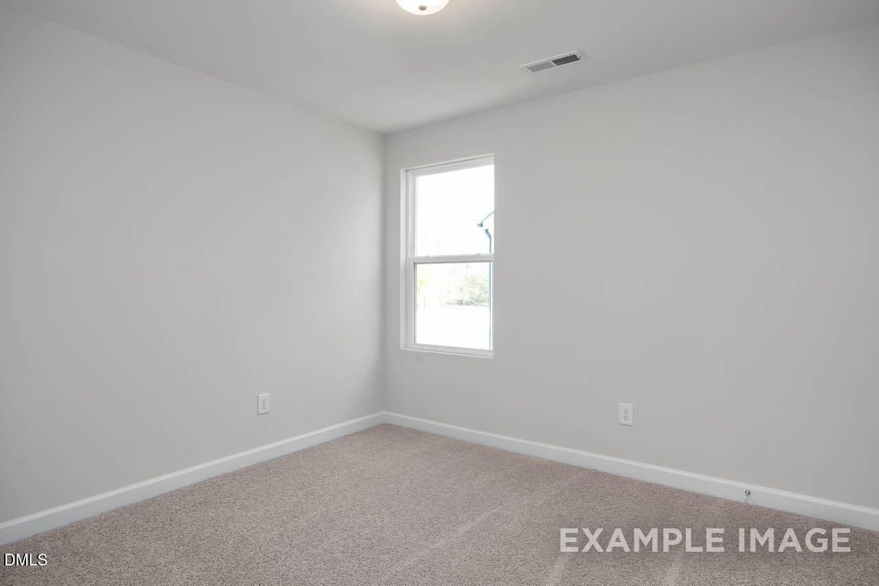 Bright empty bedroom with white walls, large window, beige carpet in Davidson Homes The Adalynn A, Lillington, NC