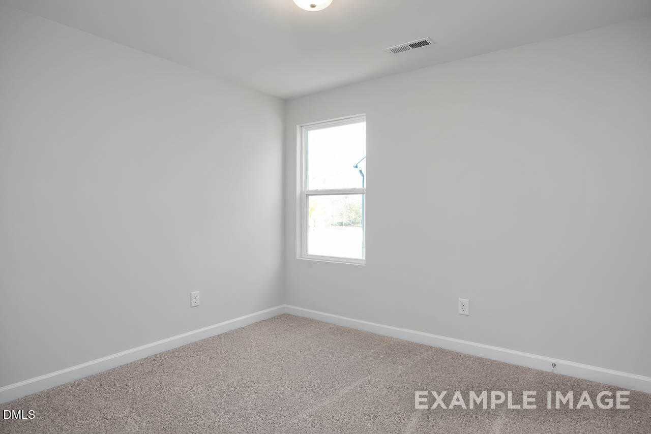 Bright empty bedroom with white walls, large window, beige carpet in Davidson Homes The Adalynn A, Lillington, NC
