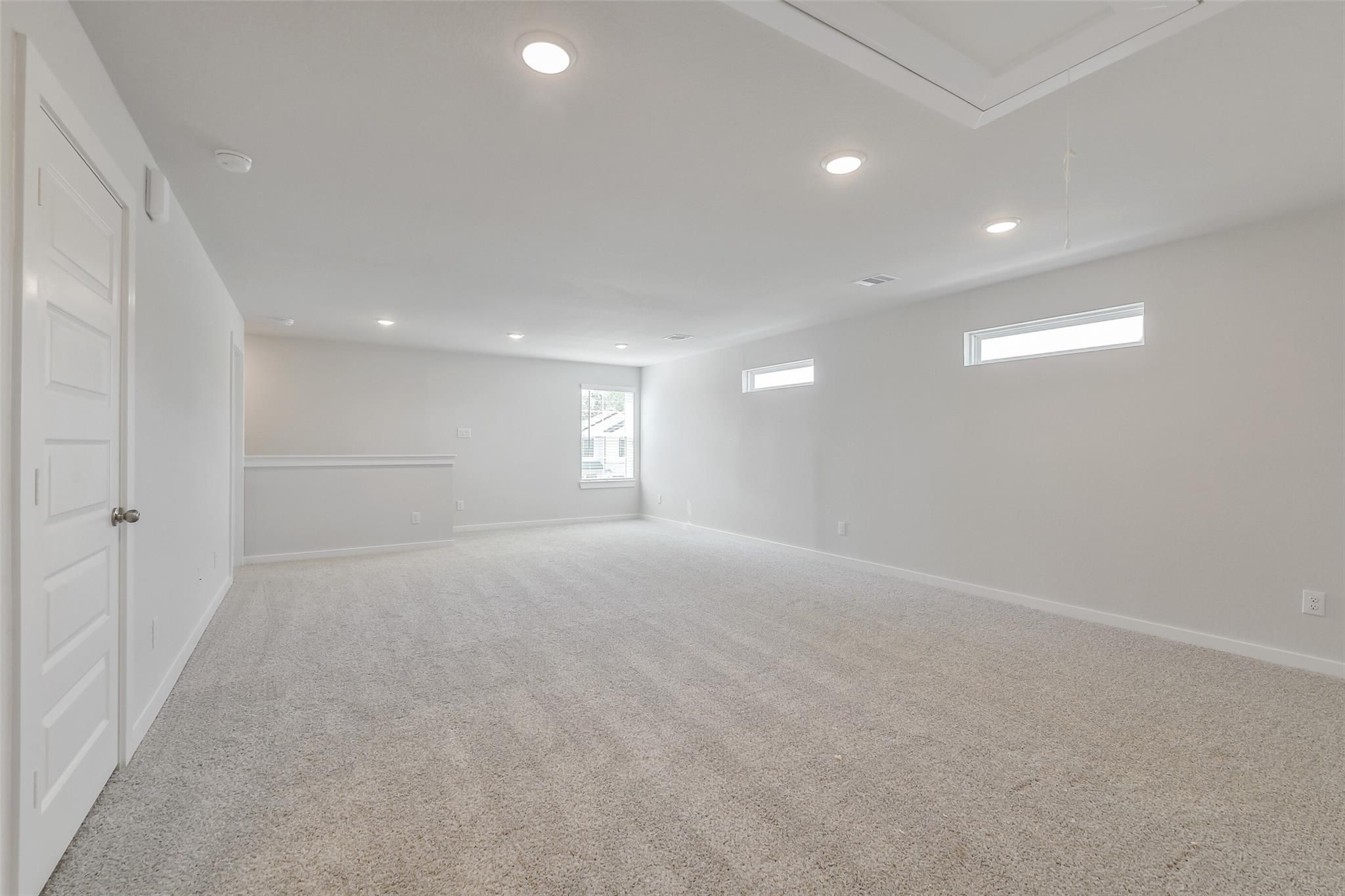 Spacious empty loft with beige carpet, white walls, recessed lighting, clerestory windows in The San Marcos E home, Conroe Texas
