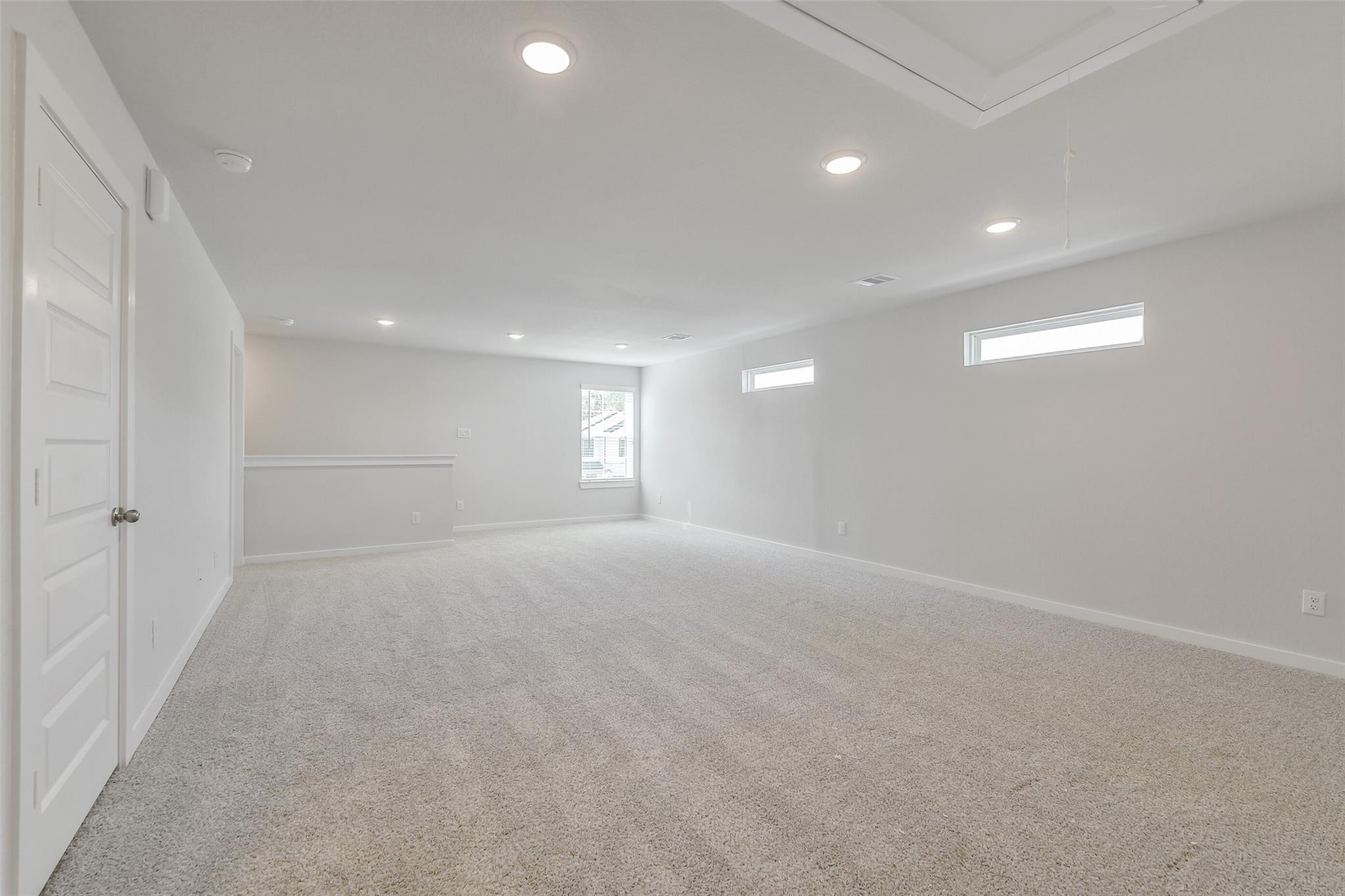 Spacious empty loft with beige carpet, white walls, recessed lighting, clerestory windows in The San Marcos E home, Conroe Texas