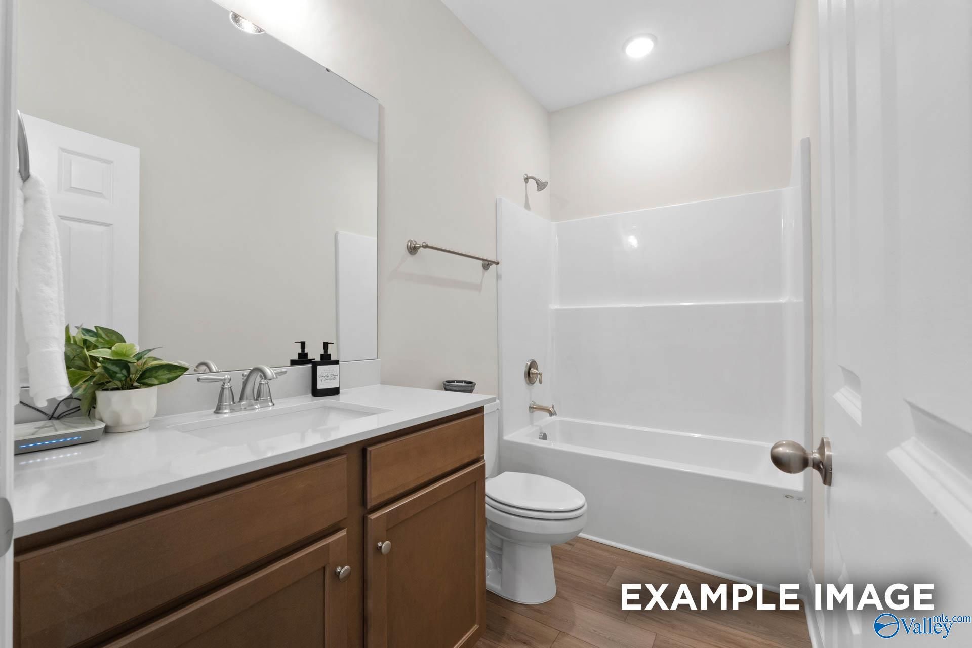 Modern bathroom with wood vanity, white countertop, and tub-shower combo in The Franklin C home at Heritage Lakes.