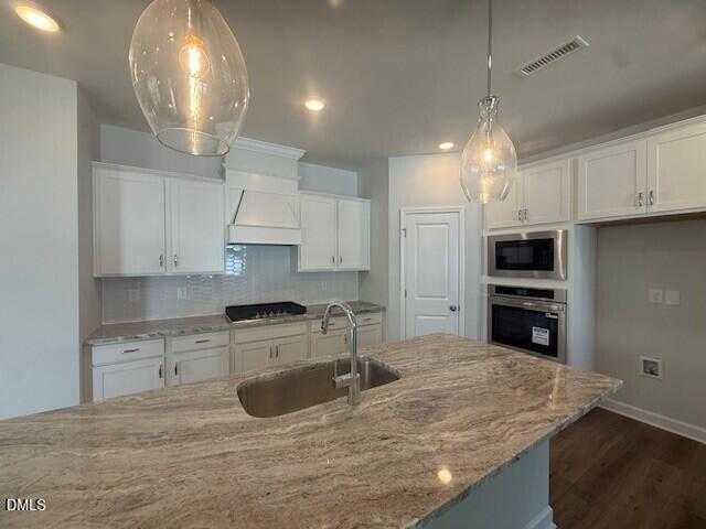 Modern kitchen featuring white shaker cabinets, speckled granite island with sink, gas cooktop, and stainless double ovens in Davidson Homes Preston C, Lillington NC