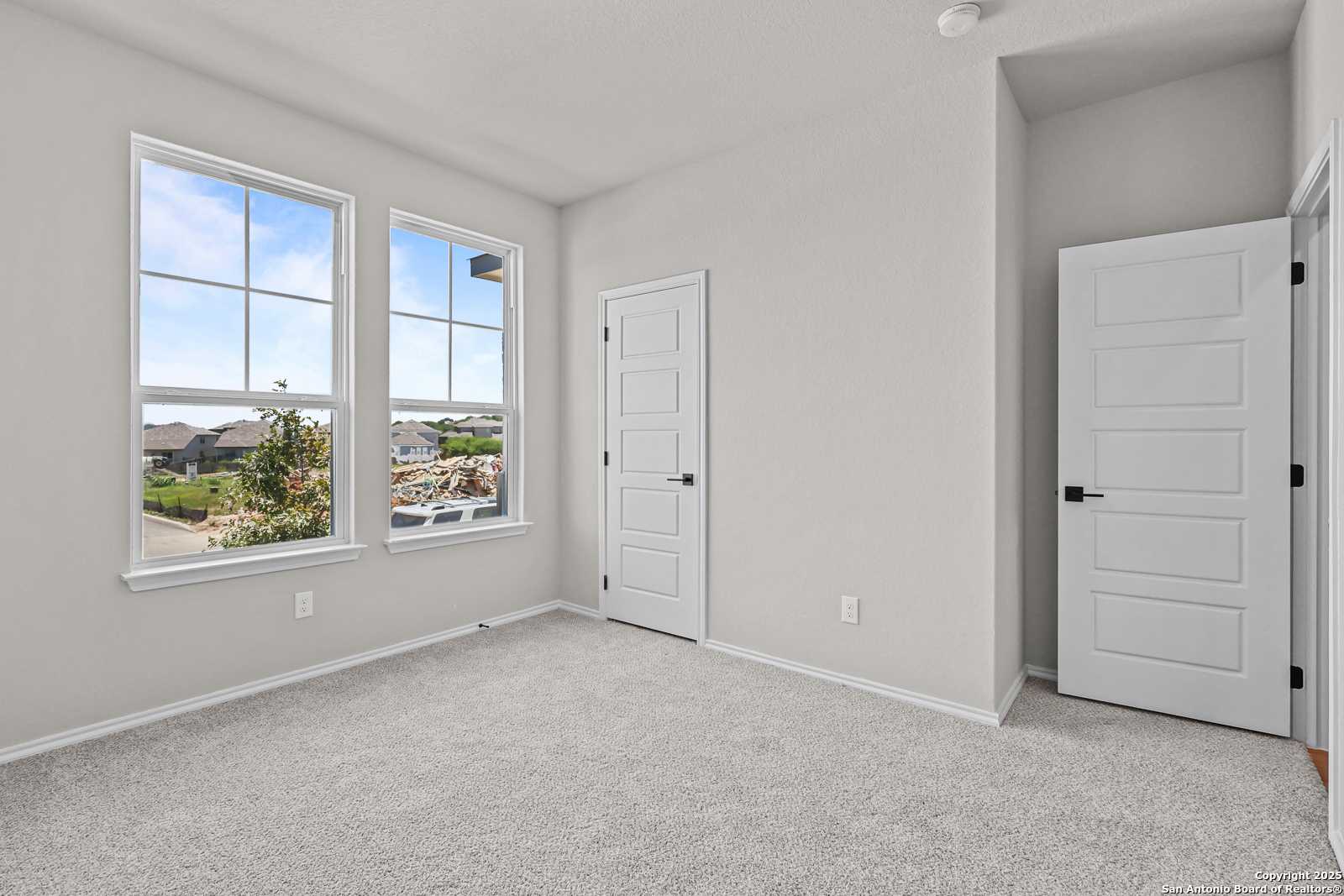 Bright secondary bedroom with large windows overlooking neighborhood, gray carpet and walls in Davidson Homes The Daphne K, San Antonio