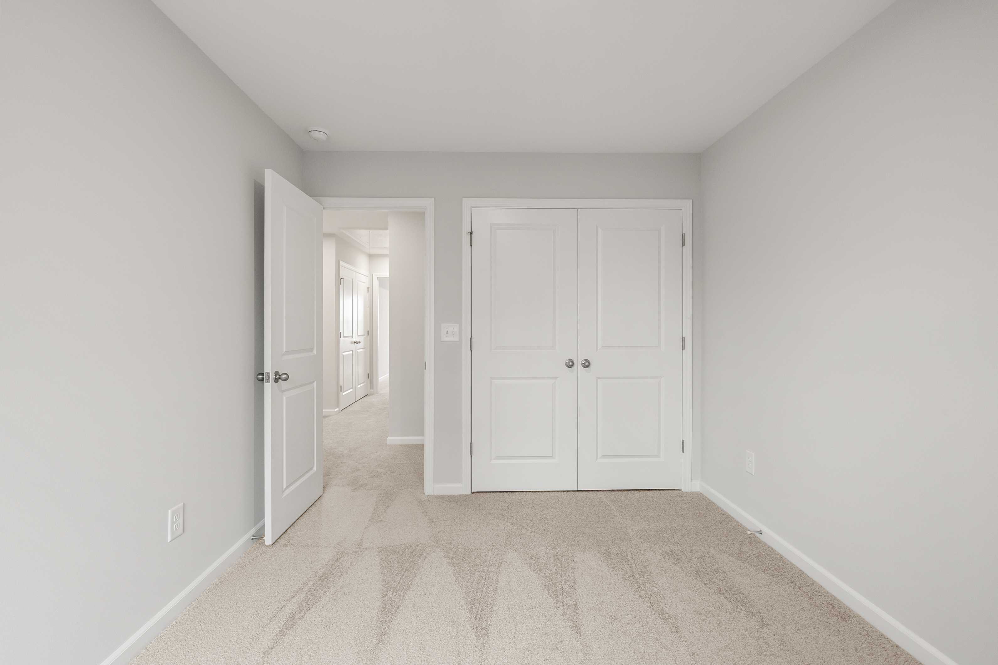 Spacious empty bedroom in The Durant A featuring light gray walls, double closet doors, and hallway view in Davidson Homes design