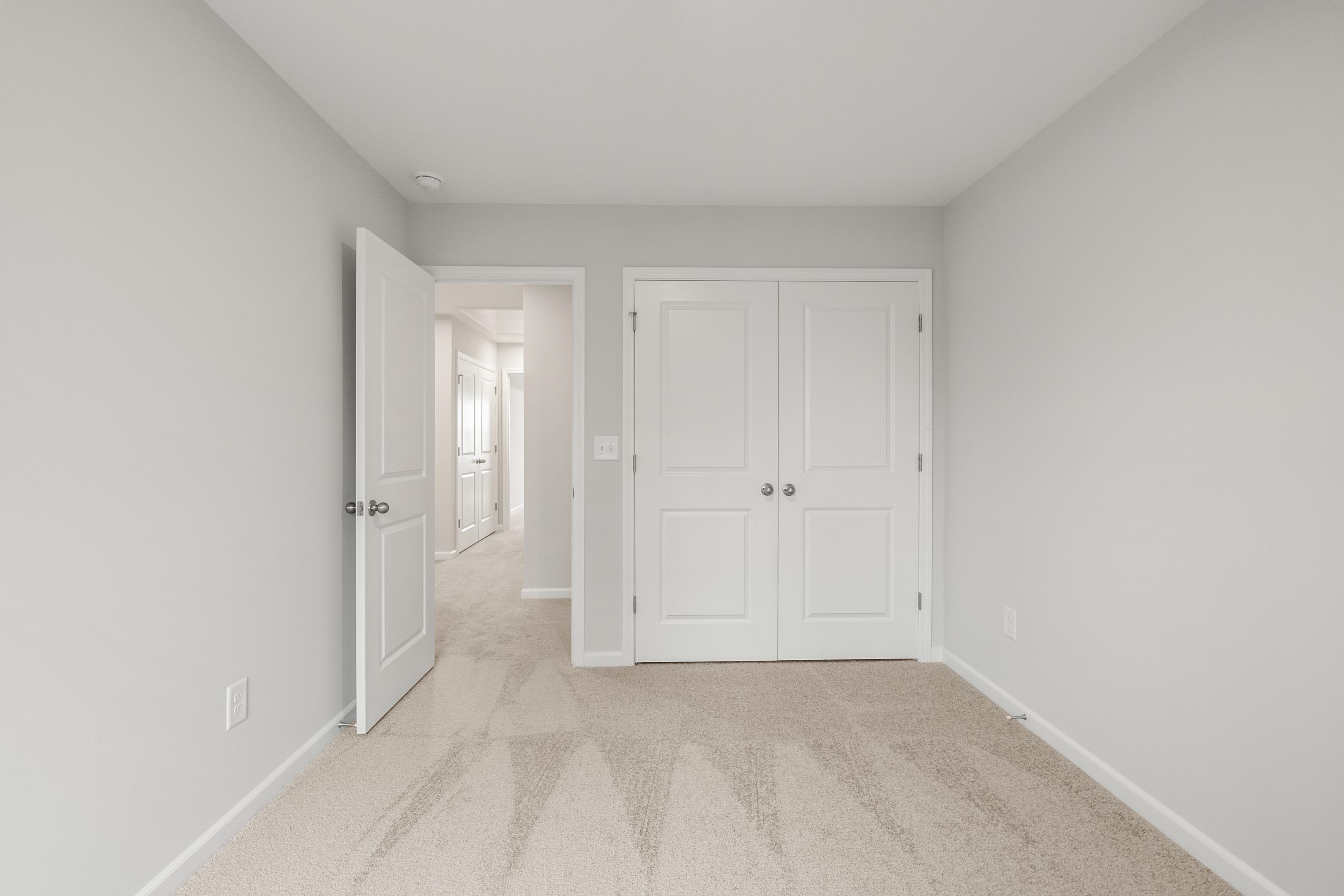 Spacious empty bedroom in The Durant A featuring light gray walls, double closet doors, and hallway view in Davidson Homes design