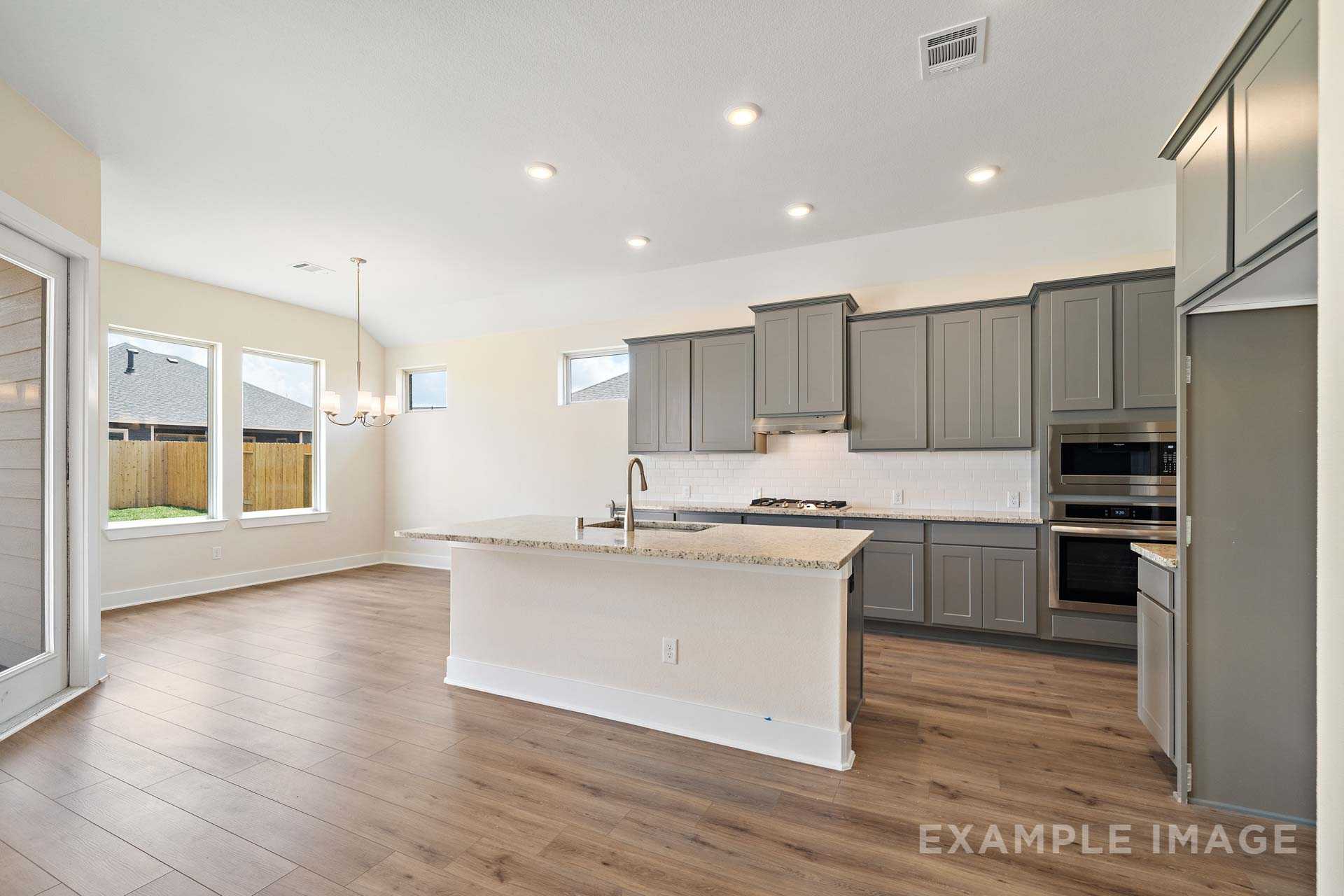 Spacious open-concept kitchen in The Diana C with gray shaker cabinets, large white island, stainless appliances, and hardwood floors