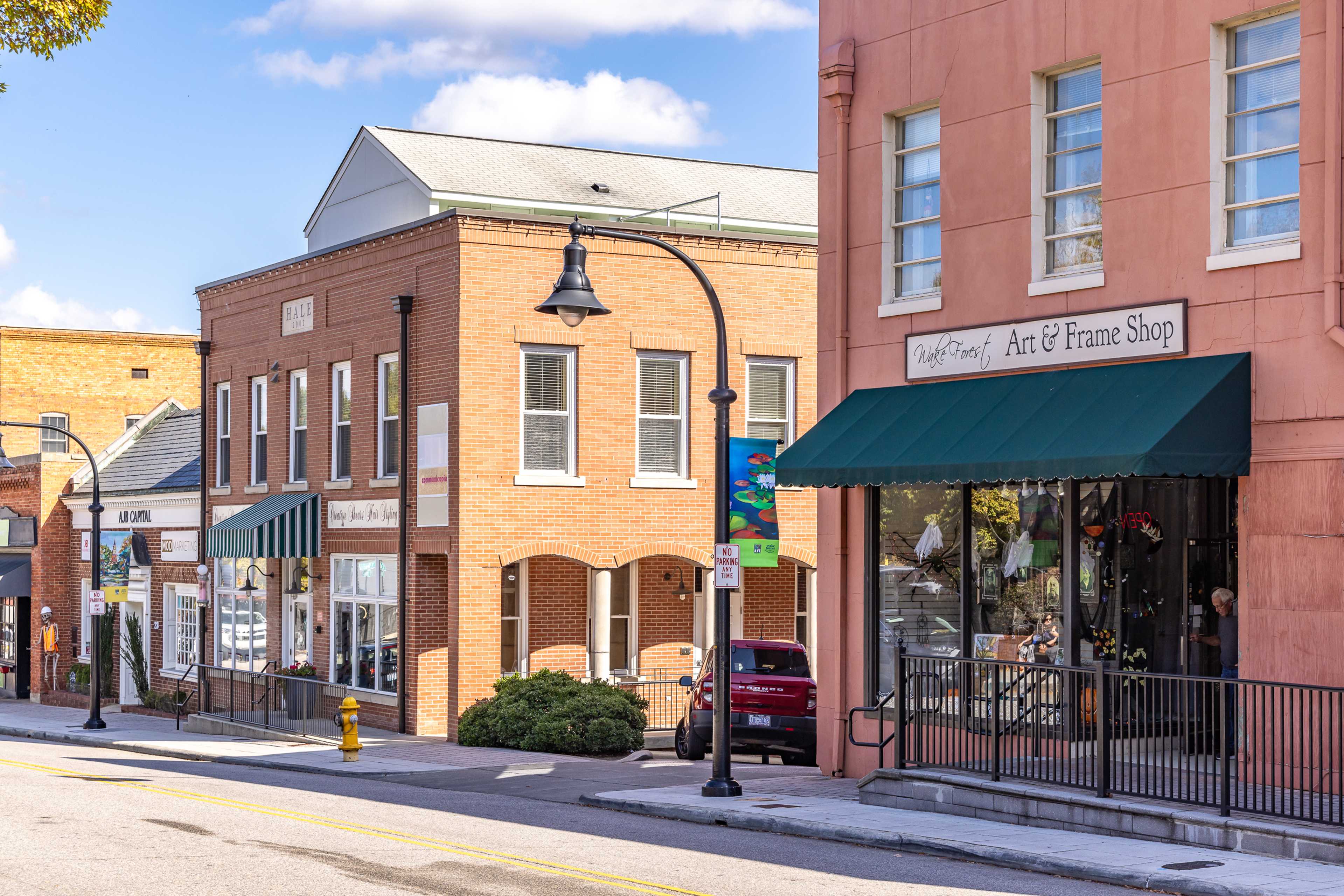 Charming brick storefronts at Sage on North Main in Wake Forest NC with art gallery, frame shop, green awnings, and street lamps