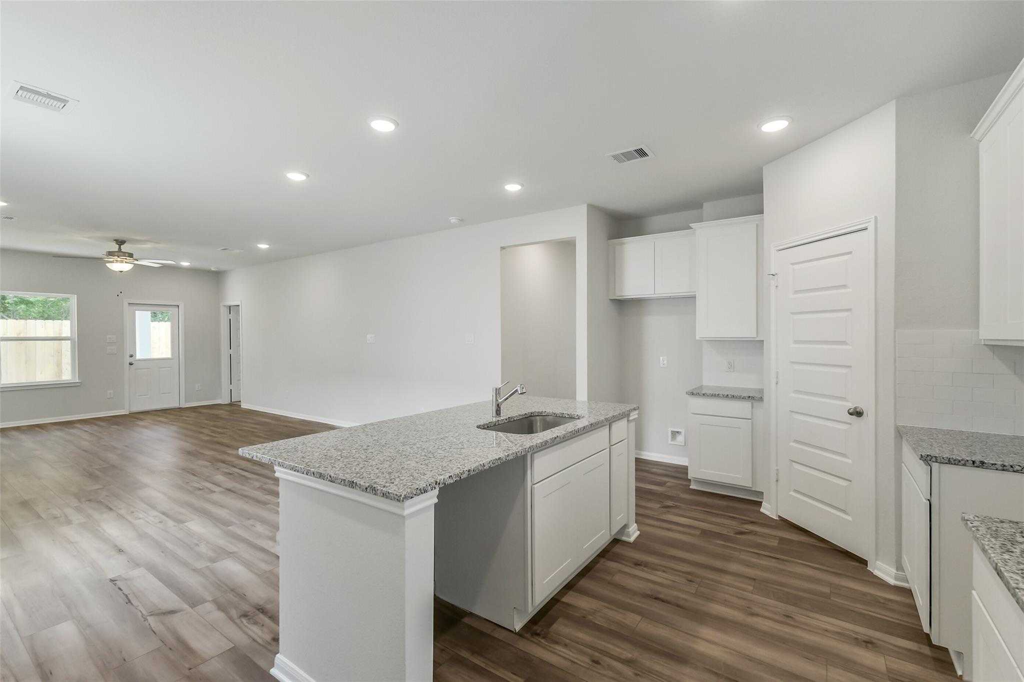 Modern open-concept kitchen with granite island sink and white cabinets in The Sabine E 4-bedroom home, Conroe, Texas