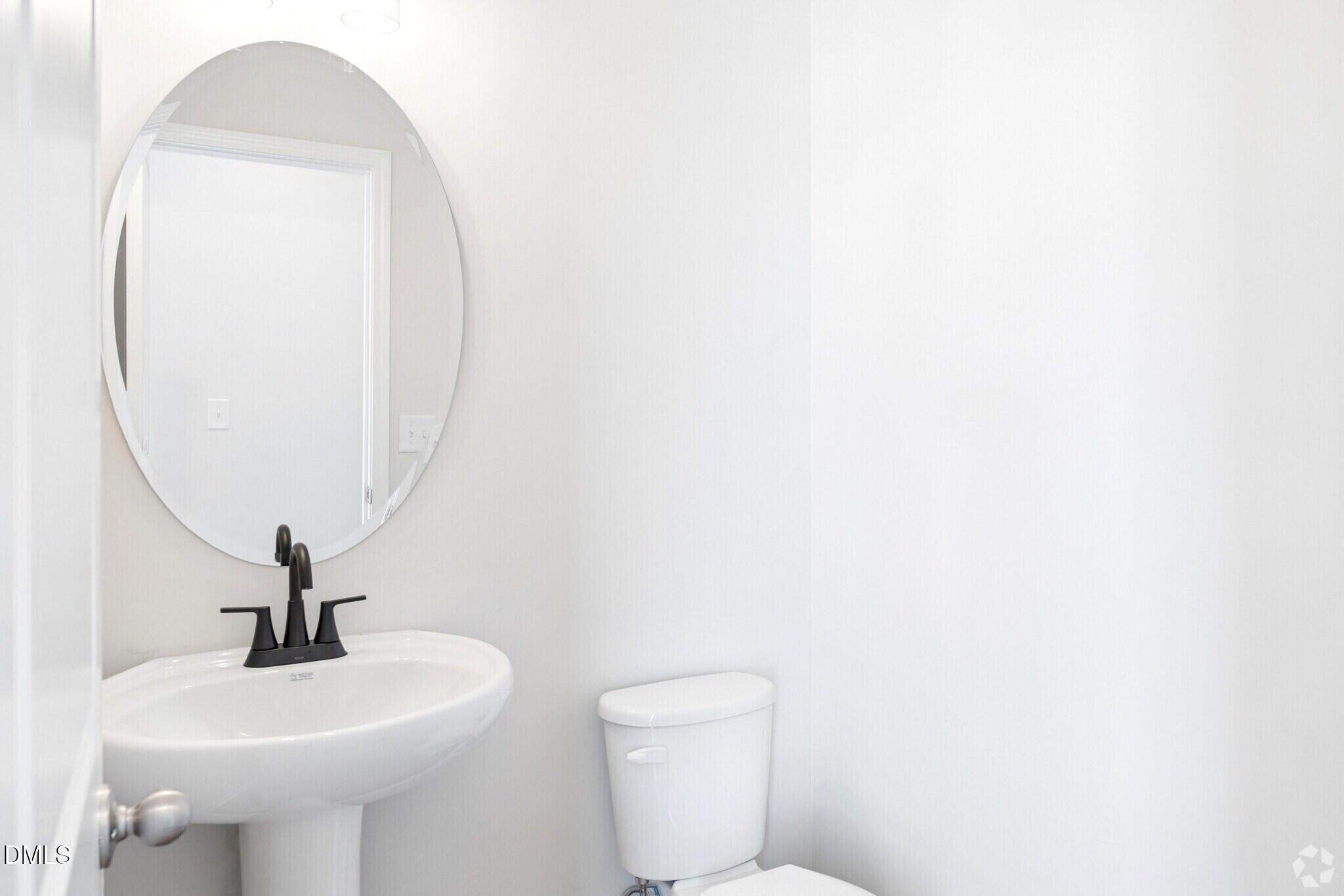 Bright white half bath with pedestal sink, round mirror, and matte black faucet in Davidson Homes The Mitchell plan, Knightdale NC