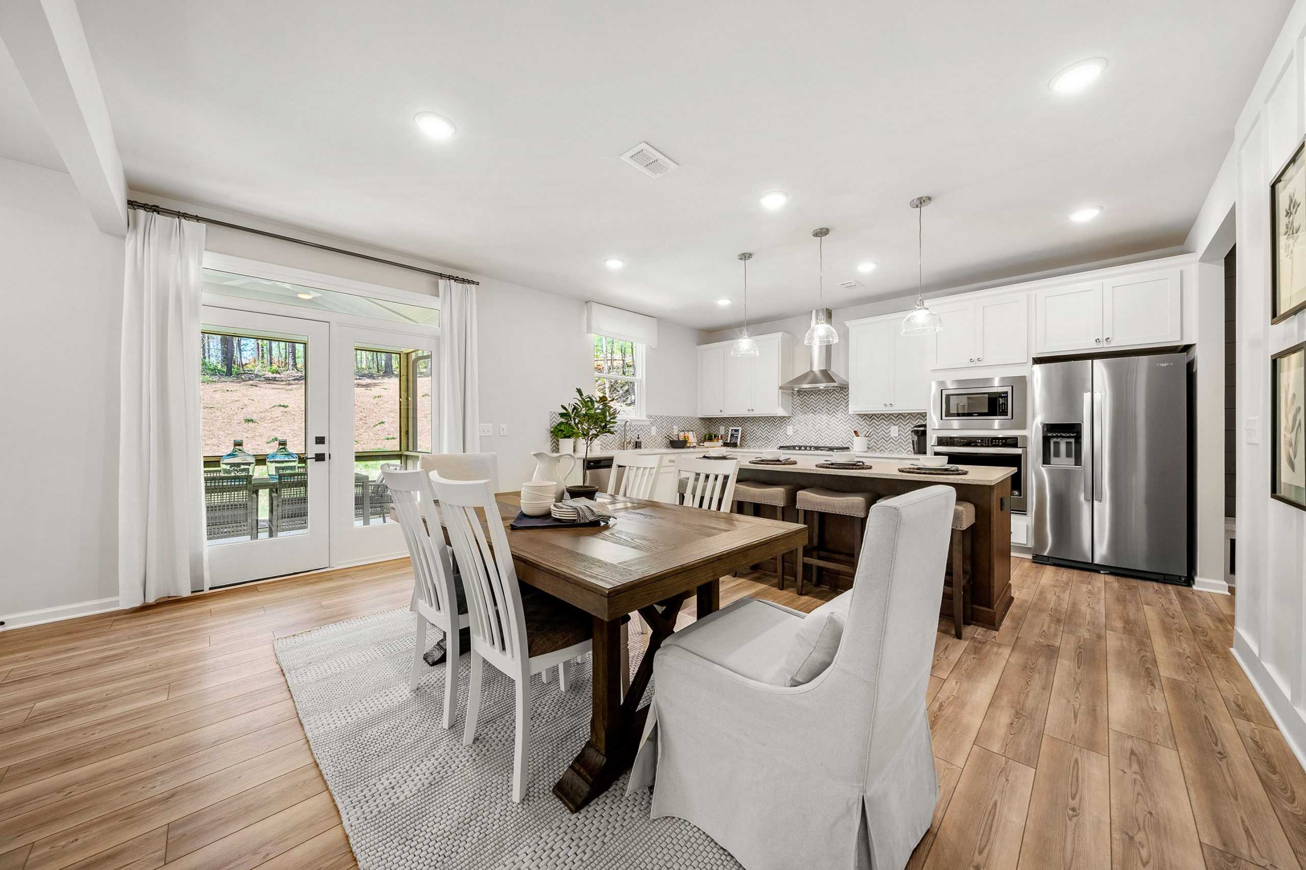 Open-concept kitchen dining area at Riverwood in Dallas Georgia with farmhouse table, white cabinets, stainless appliances, hardwood floors