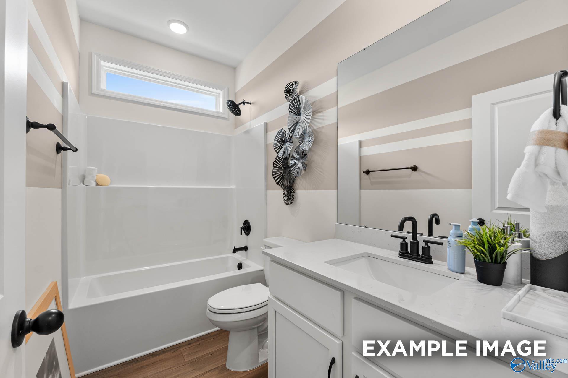 Modern bathroom with white vanity, tub-shower combo, and striped walls in The Franklin D home at Berry Cove, New Market, AL.